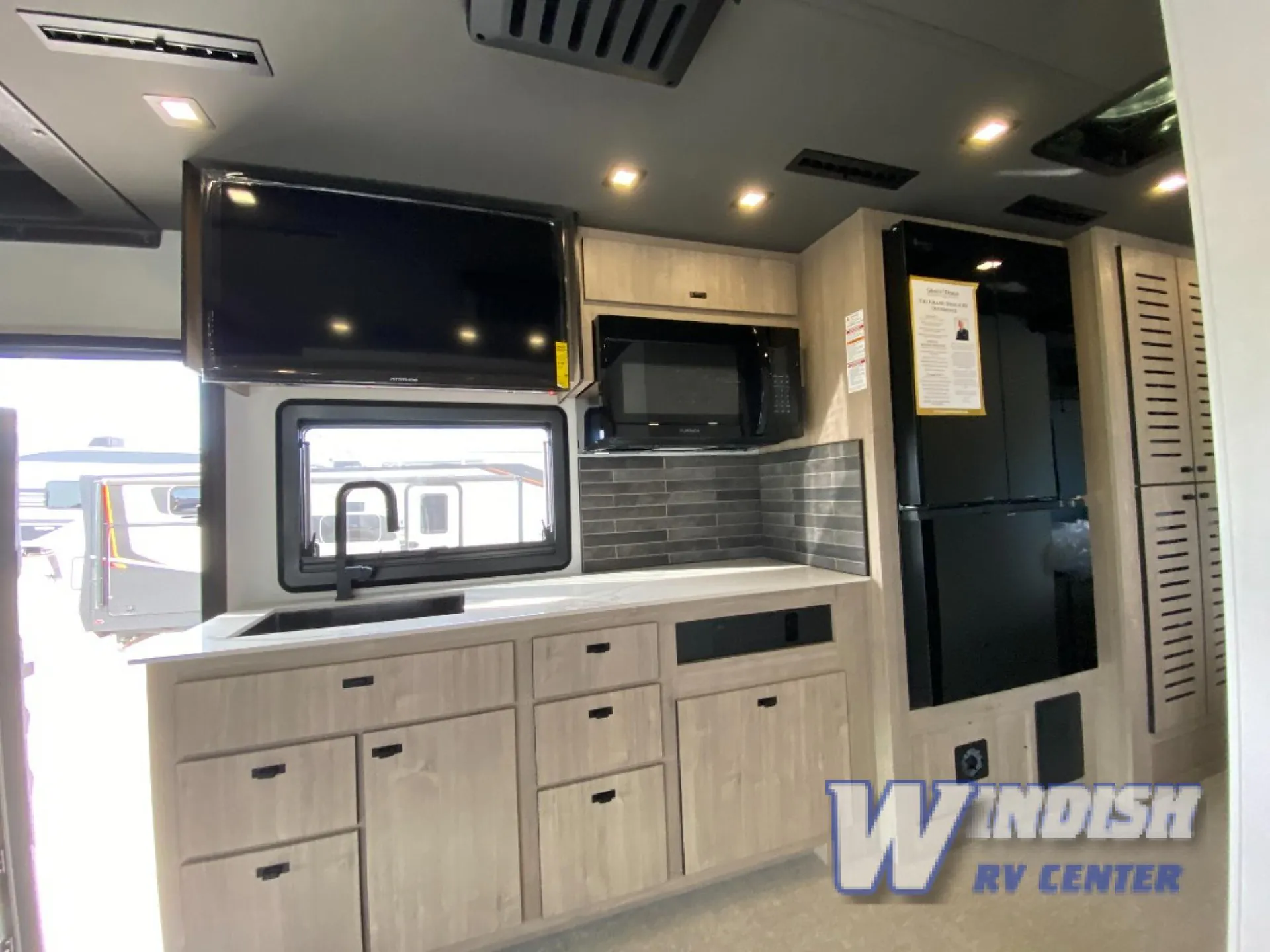 2027 Grand Design Lineage Series F 29AN5 — Motorhome kitchen with sink, microwave, refrigerator, dark backsplash, cabinets, and a television above the window