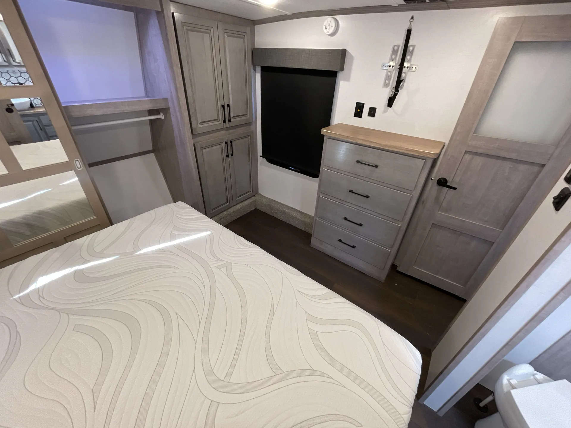 2023 Dutchmen Voltage 4225 — Bedroom view showing the main bed, television, dresser, tall wardrobe cabinets, and mirrored closet door