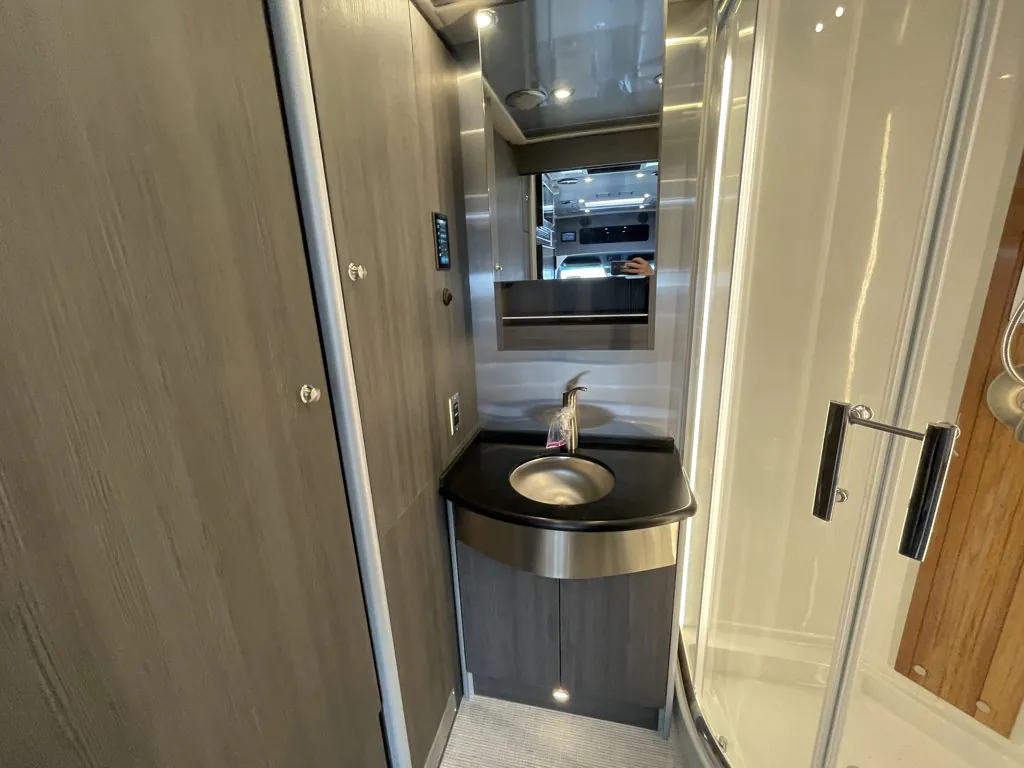 2026 Airstream Atlas Murphy Suite — Bathroom vanity and sink beside a glass shower enclosure with reflective medicine cabinet