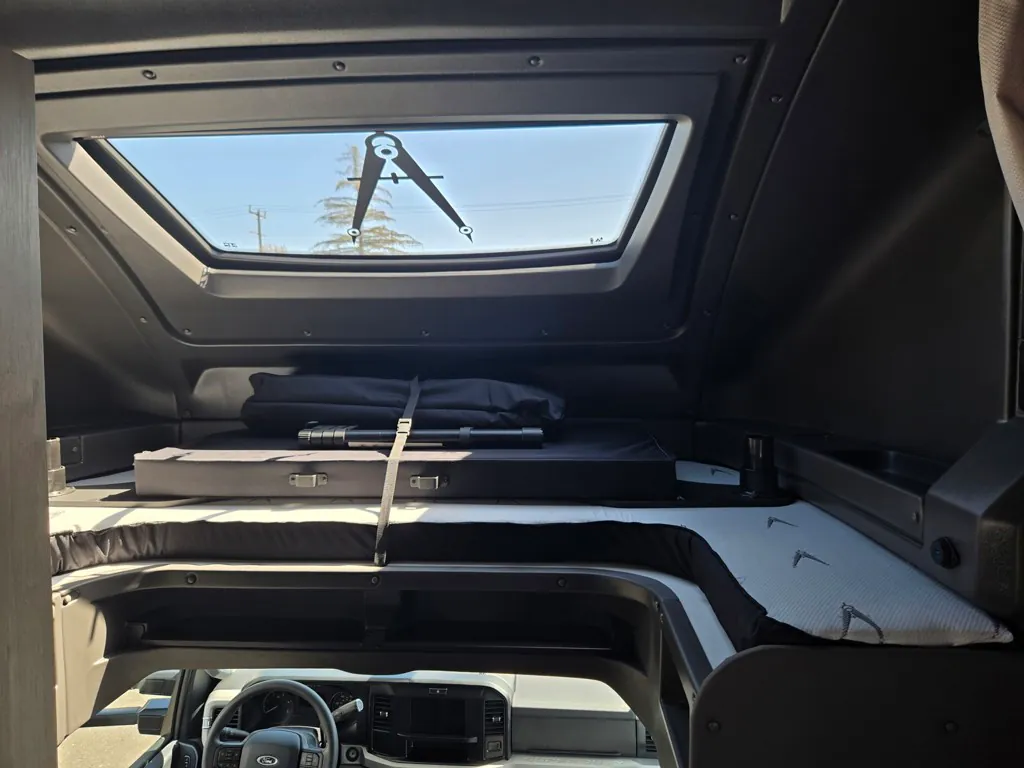 2027 Grand Design Lineage Series F 29AN5 — Over-cab sleeping platform with mattress and skylight above the visible driver cockpit and steering wheel