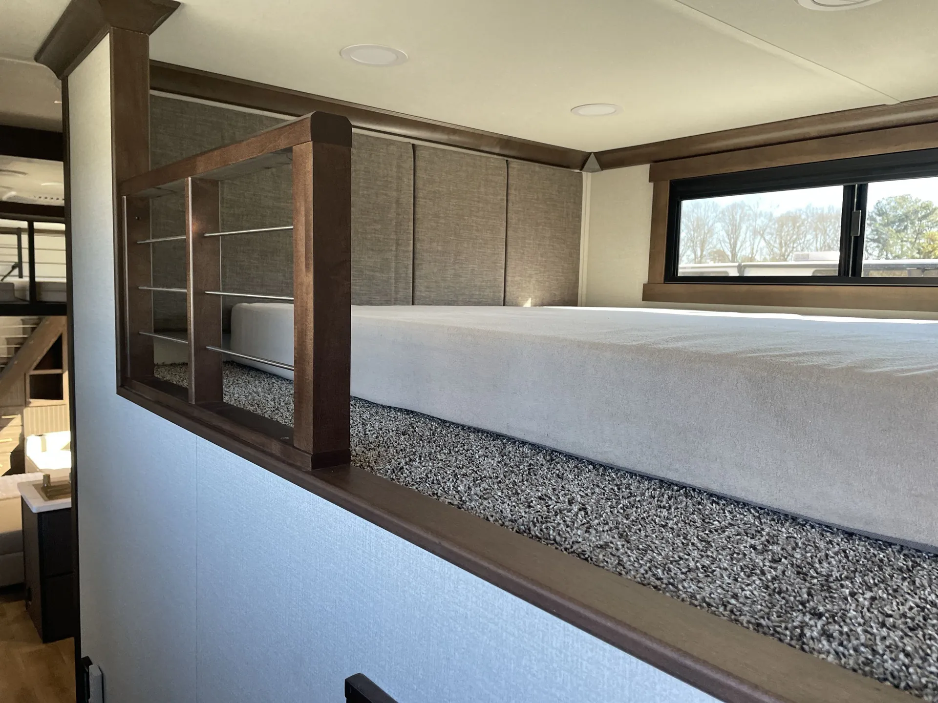 2026 Forest River Cedar Creek Cottage 41FWC — Elevated overhead sleeping platform with mattress, padded wall, open shelving, window, and access overlooking the living area