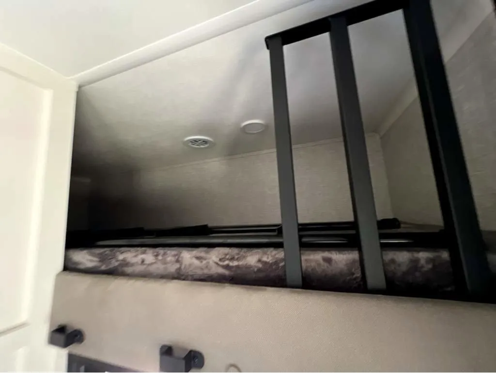 2025 Jayco Seismic Luxury Series 4113 — Over-cab loft sleeping platform with mattress, black safety rails, ladder, and ceiling vents