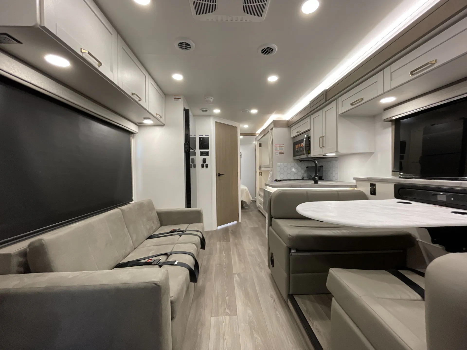 2027 Jayco Alante 29F — Class A motorhome lounge with sofa, booth seating, kitchen counters, overhead cabinets, and central aisle