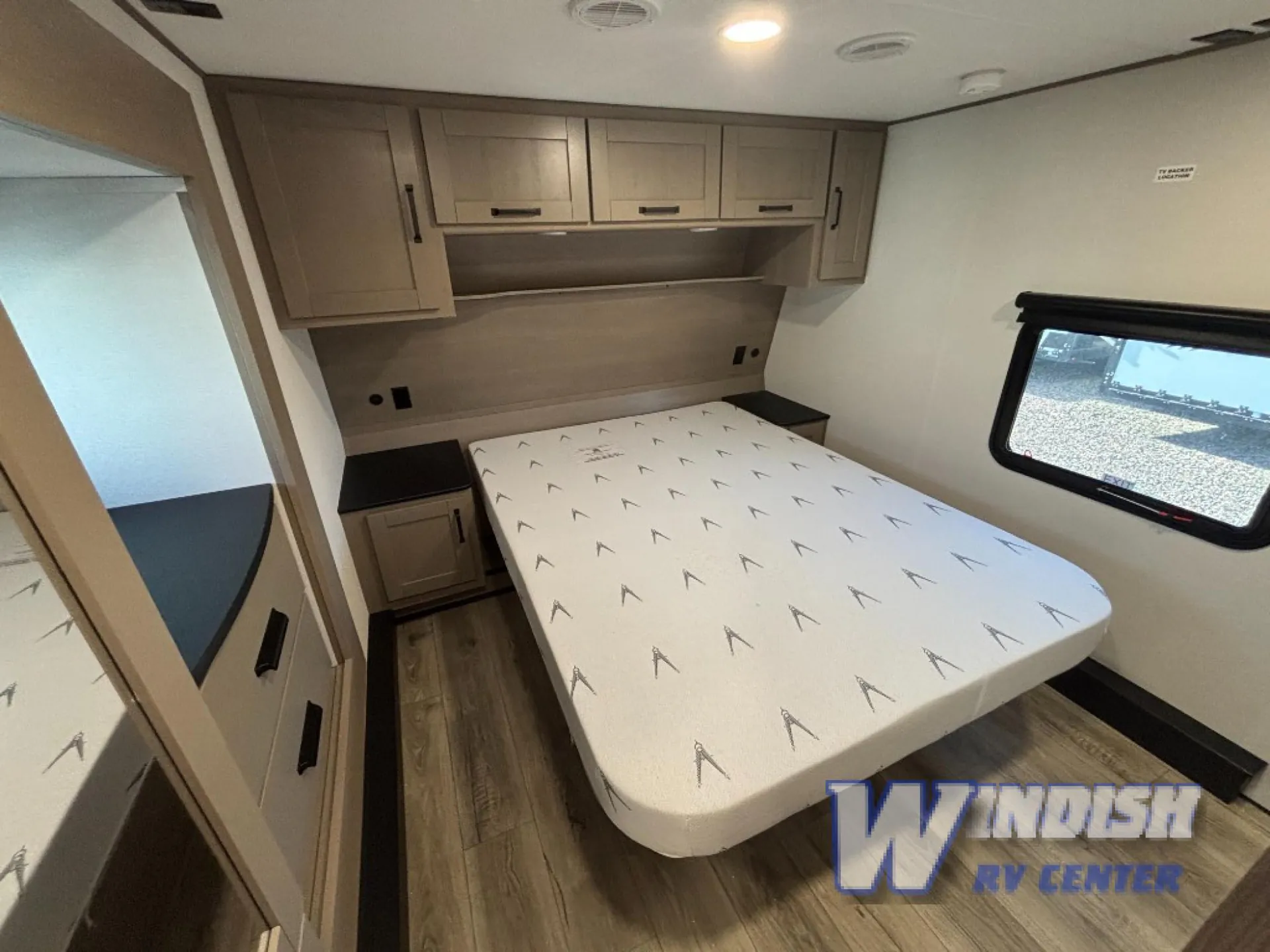 2027 Grand Design Reflection 362TBS — Main bedroom with a centered bed, overhead cabinets, bedside surfaces, dresser storage, and a window