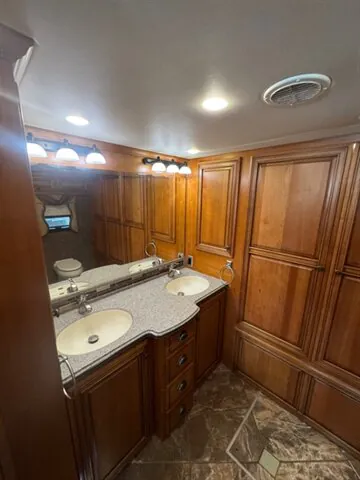 2016 Newmar Dutch Star 4369 — Bathroom vanity with dual sinks, mirrored medicine cabinet, wood cabinetry, and a toilet at the edge