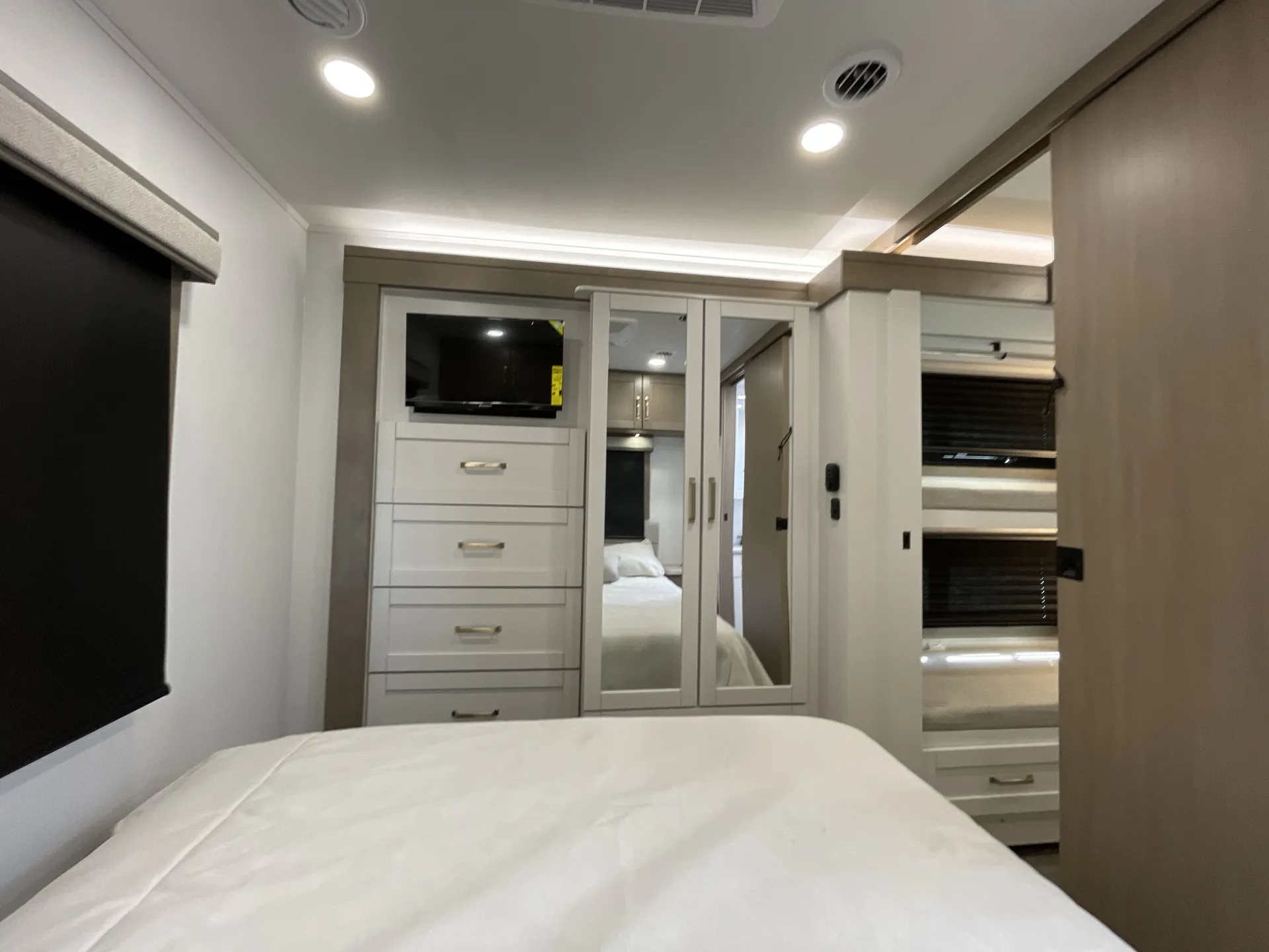 2027 Jayco Alante 29F — Bedroom view showing the bed, mirrored wardrobe doors, dresser drawers, overhead cabinets, and window shades