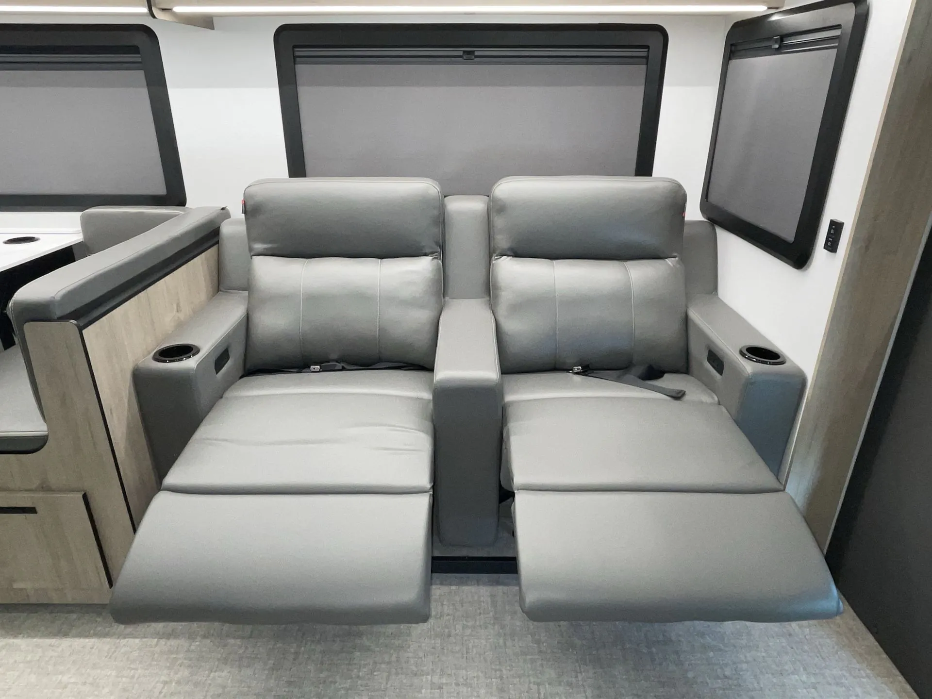 2027 Grand Design Lineage Series F 31ZW — Two gray theater recliners are extended into footrests beneath shaded windows in the lounge