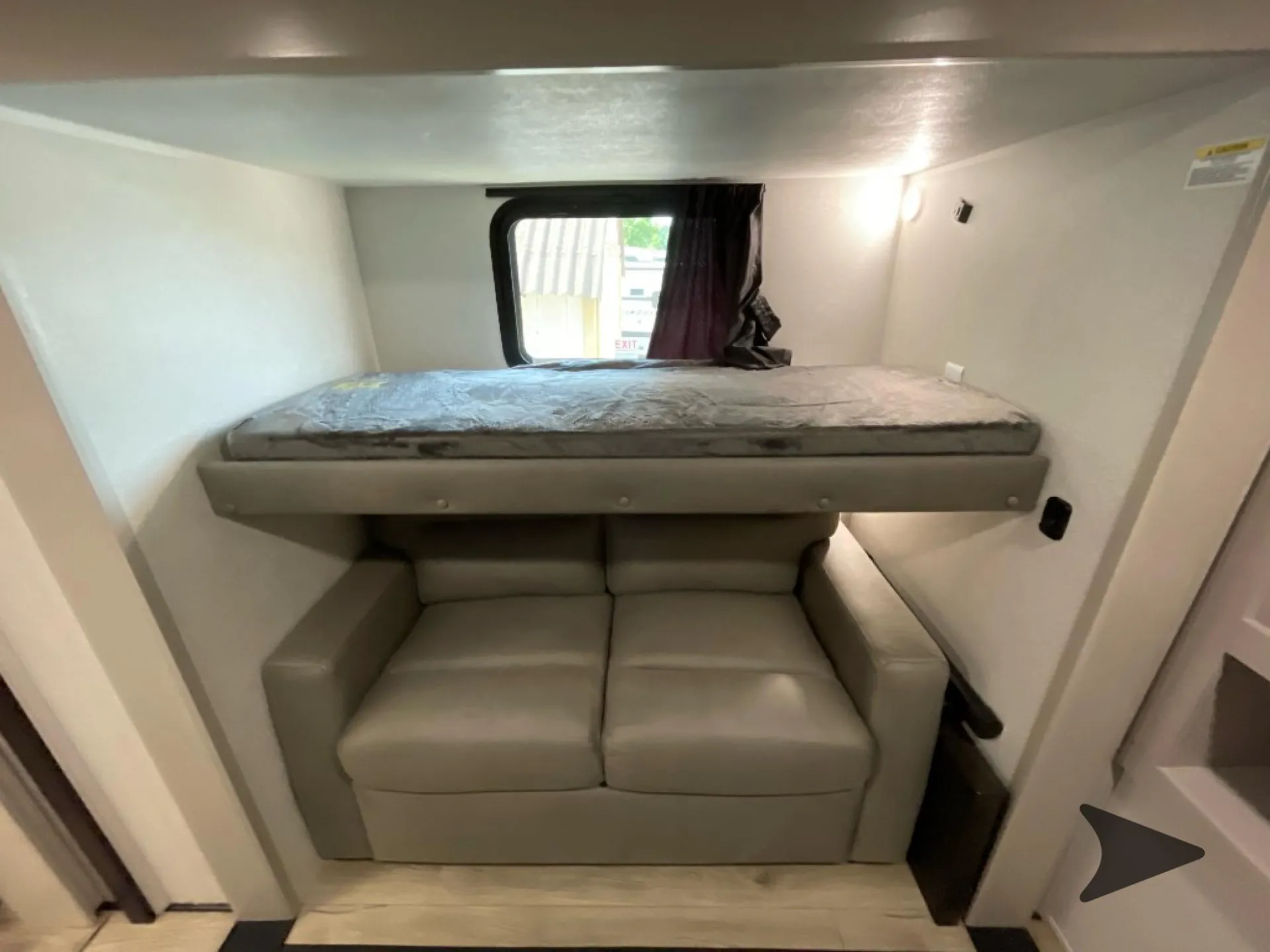 2026 Jayco North Point 377RLBH — Over-cab loft bed positioned above a two-seat sofa, with a window behind the mattress