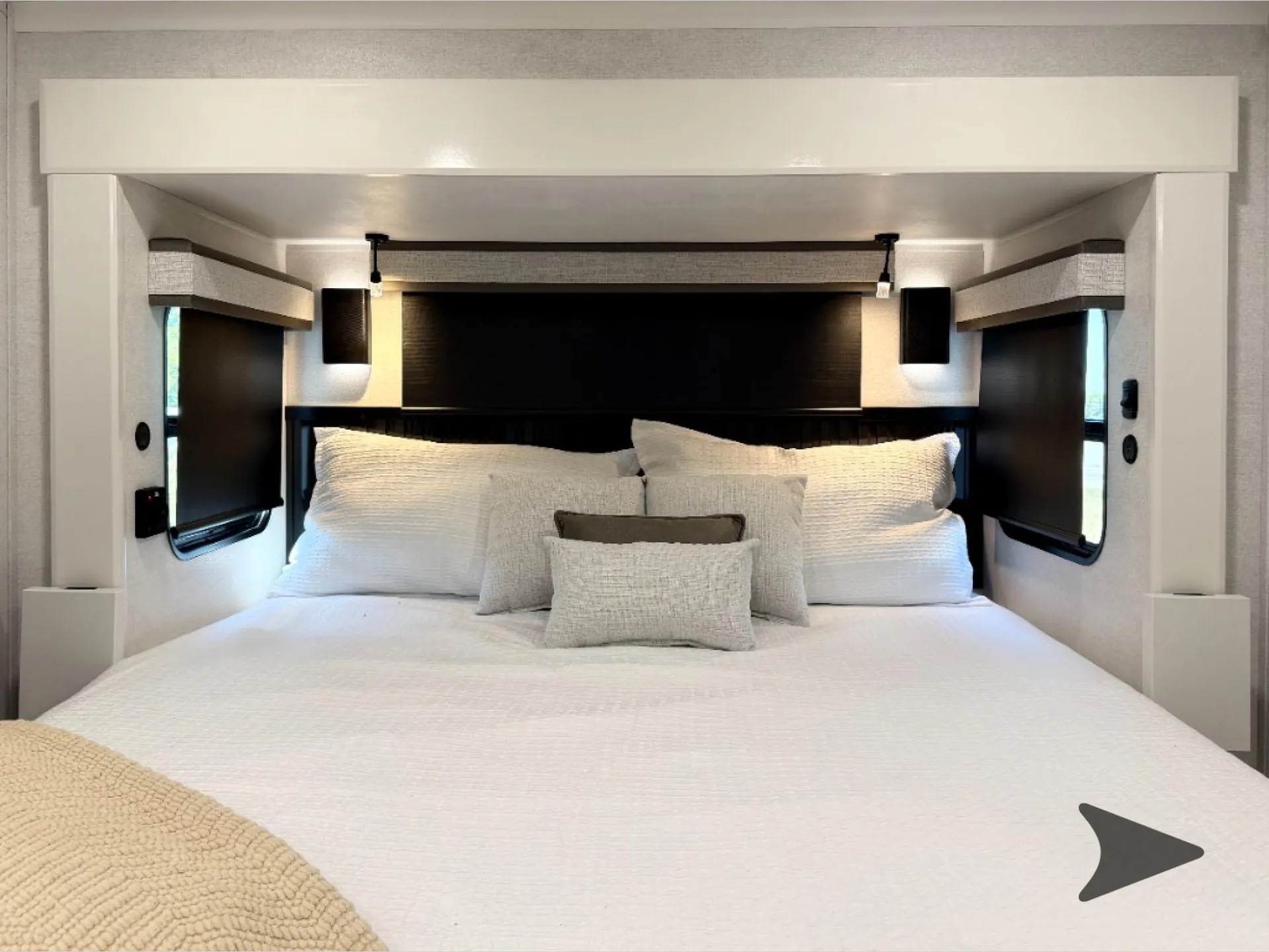 2027 Jayco Pinnacle 39FLOK — Main bedroom bed with pillows, side windows, overhead cabinetry, and a wall-mounted television