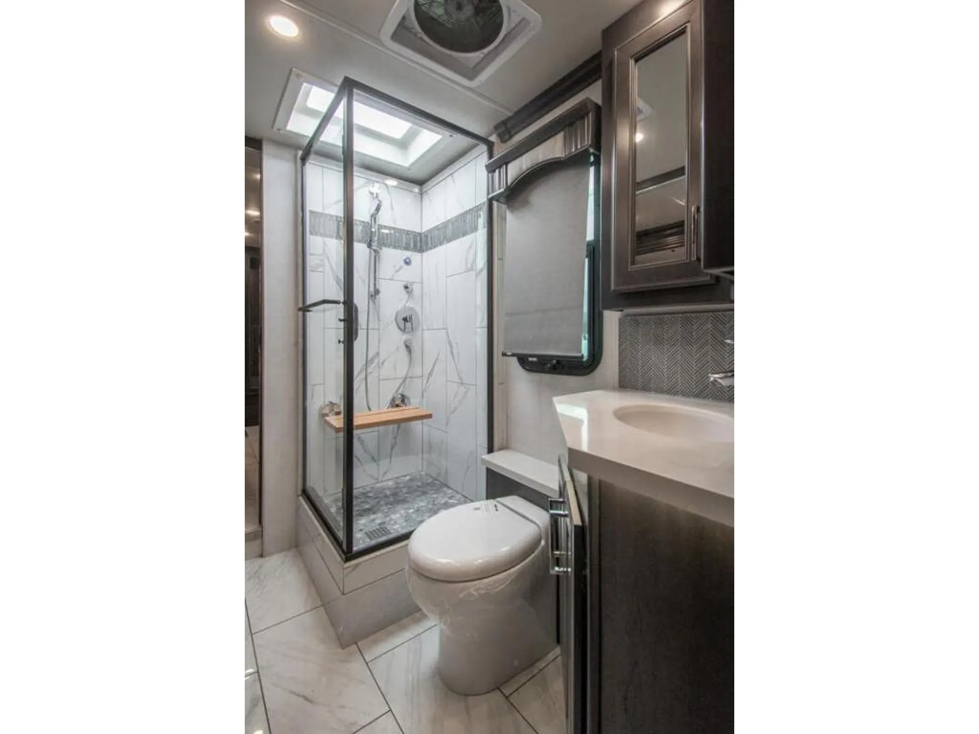 2026 Fleetwood Discovery LXE 40G — Motorhome bathroom contains a glass shower, toilet, vanity sink, storage cabinet, and roof vent