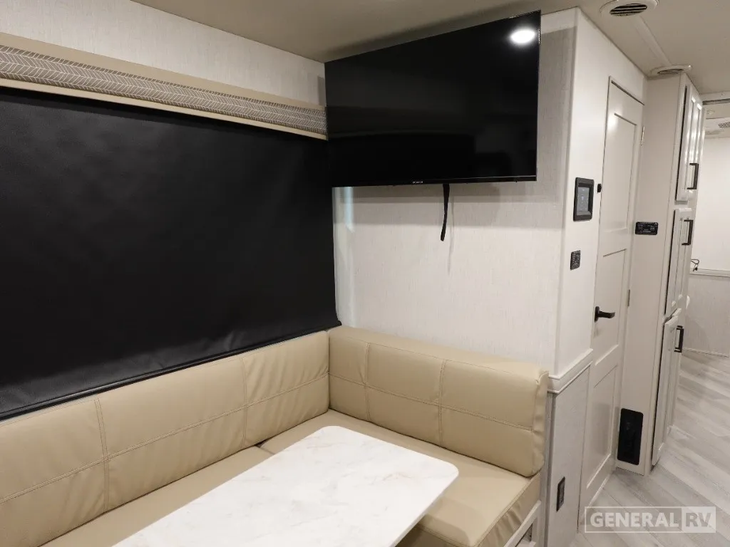 2026 Holiday Rambler Invicta 36Y — Corner dinette with table beside a lounge area, wall-mounted television, and hallway cabinetry