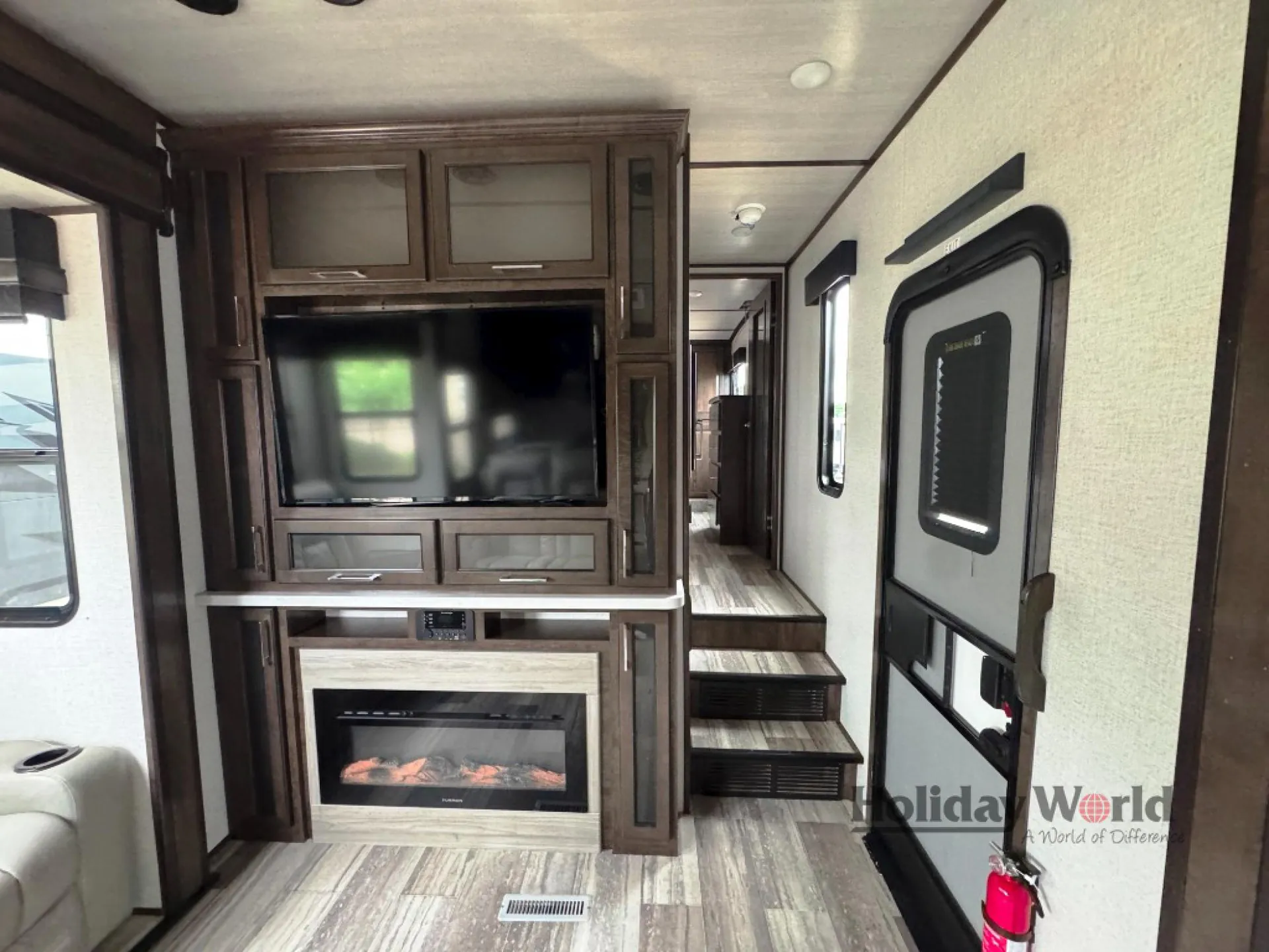 2022 Dutchmen Voltage 4225 — Living-area entertainment center with television, fireplace, surrounding cabinets, steps, and entry door
