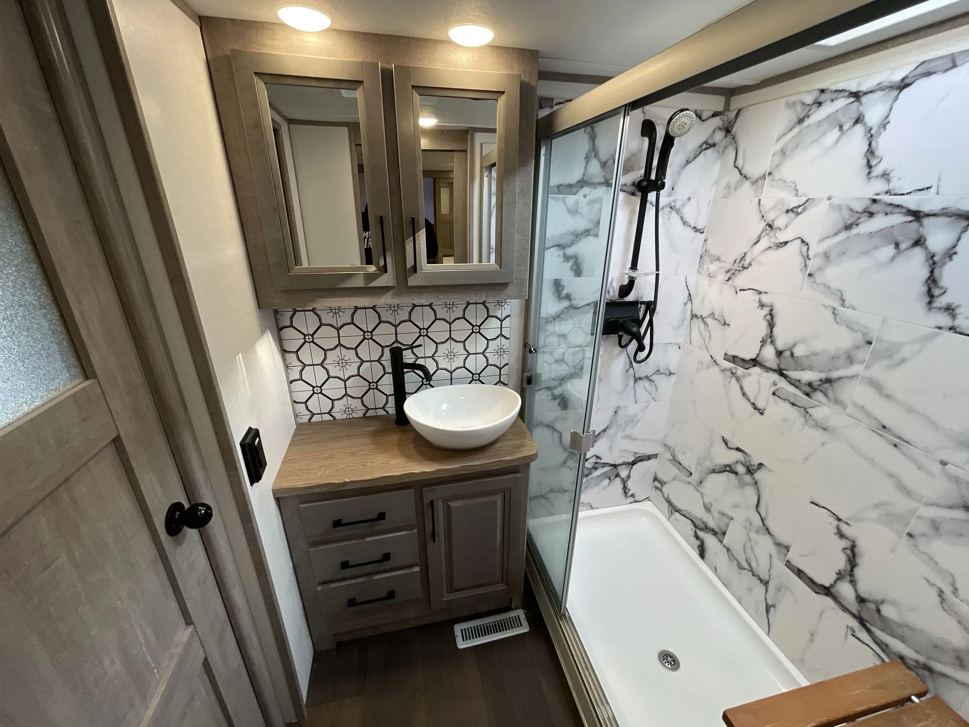 2023 Dutchmen Voltage 4225 — Bathroom vanity with vessel sink, mirrored medicine cabinets, patterned backsplash, and adjacent glass-enclosed shower