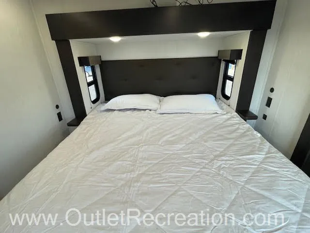 2026 Forest River Arctic Wolf 38LEAH.G — Main bedroom with a king bed, padded headboard, bedside ledges, windows, and overhead projector shelf