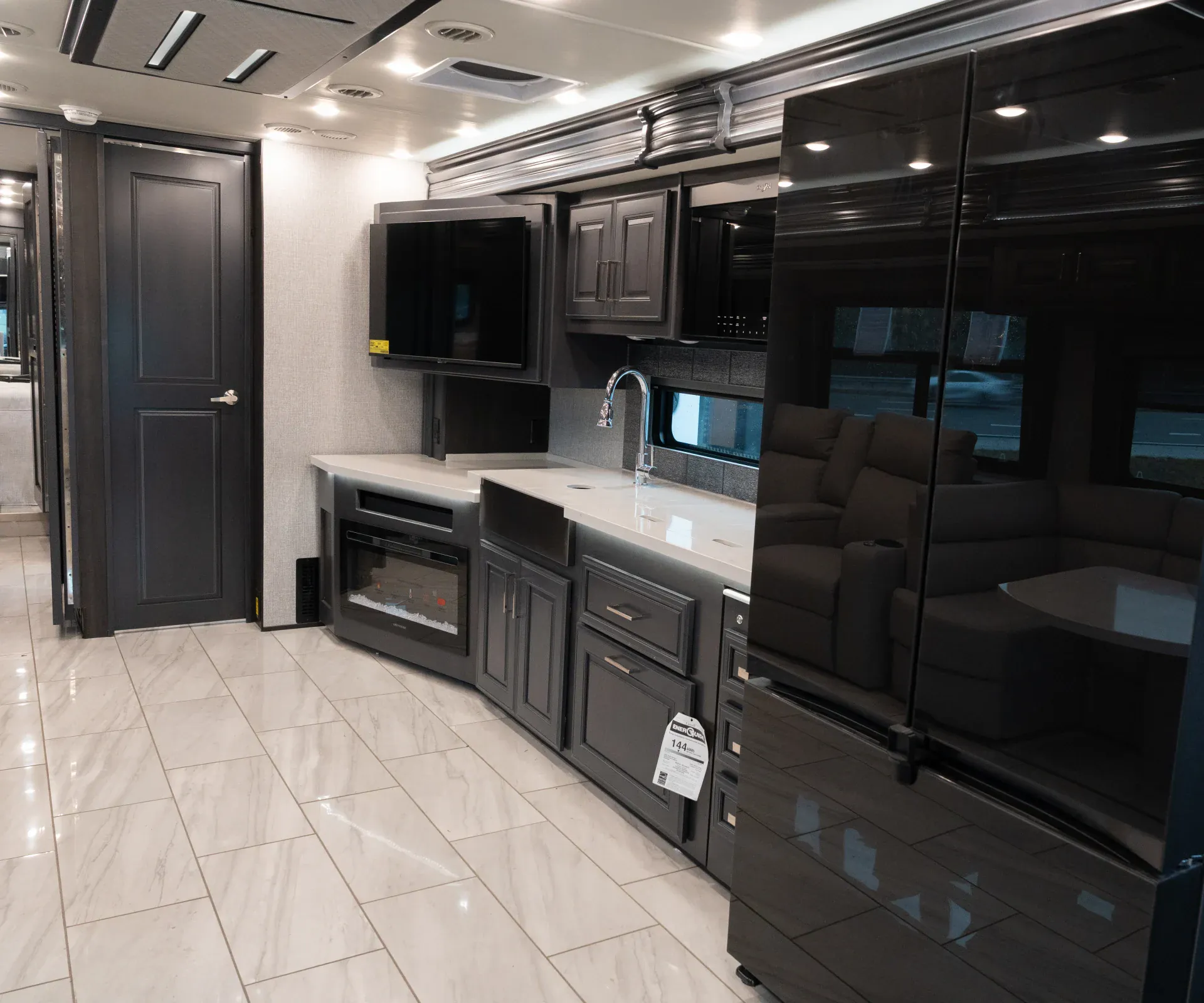 2026 Fleetwood Discovery LXE 40G — Kitchen wall with refrigerator, sink, counter, cabinetry, and television beside the visible lounge seating