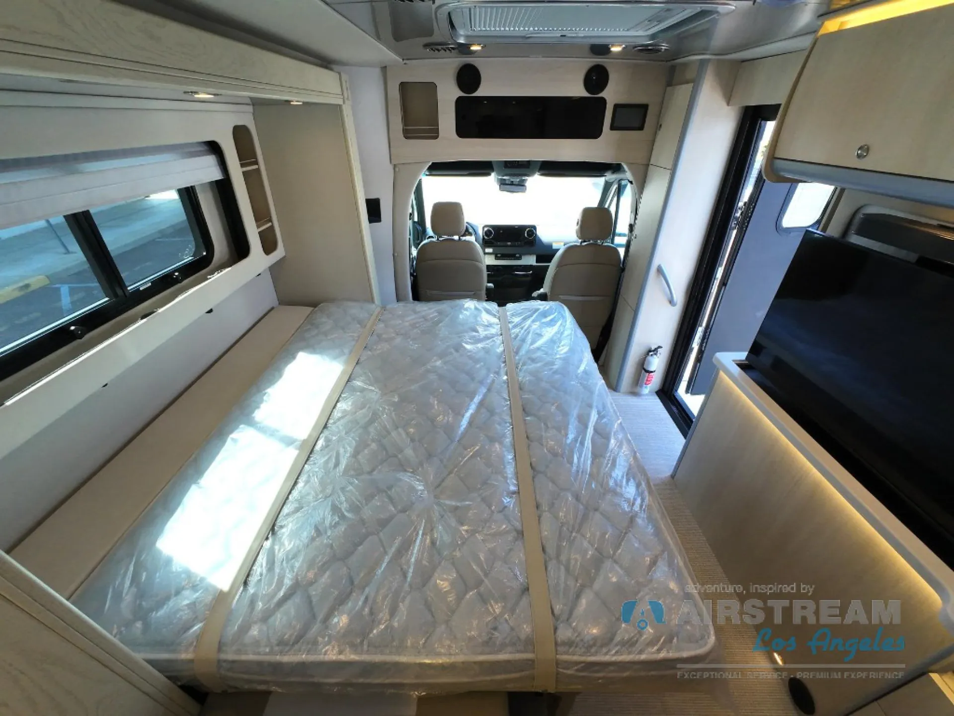 2026 Airstream Atlas Murphy Suite — Main bed extends toward the cab, with driver and passenger seats and dashboard controls visible beyond the sleeping platform