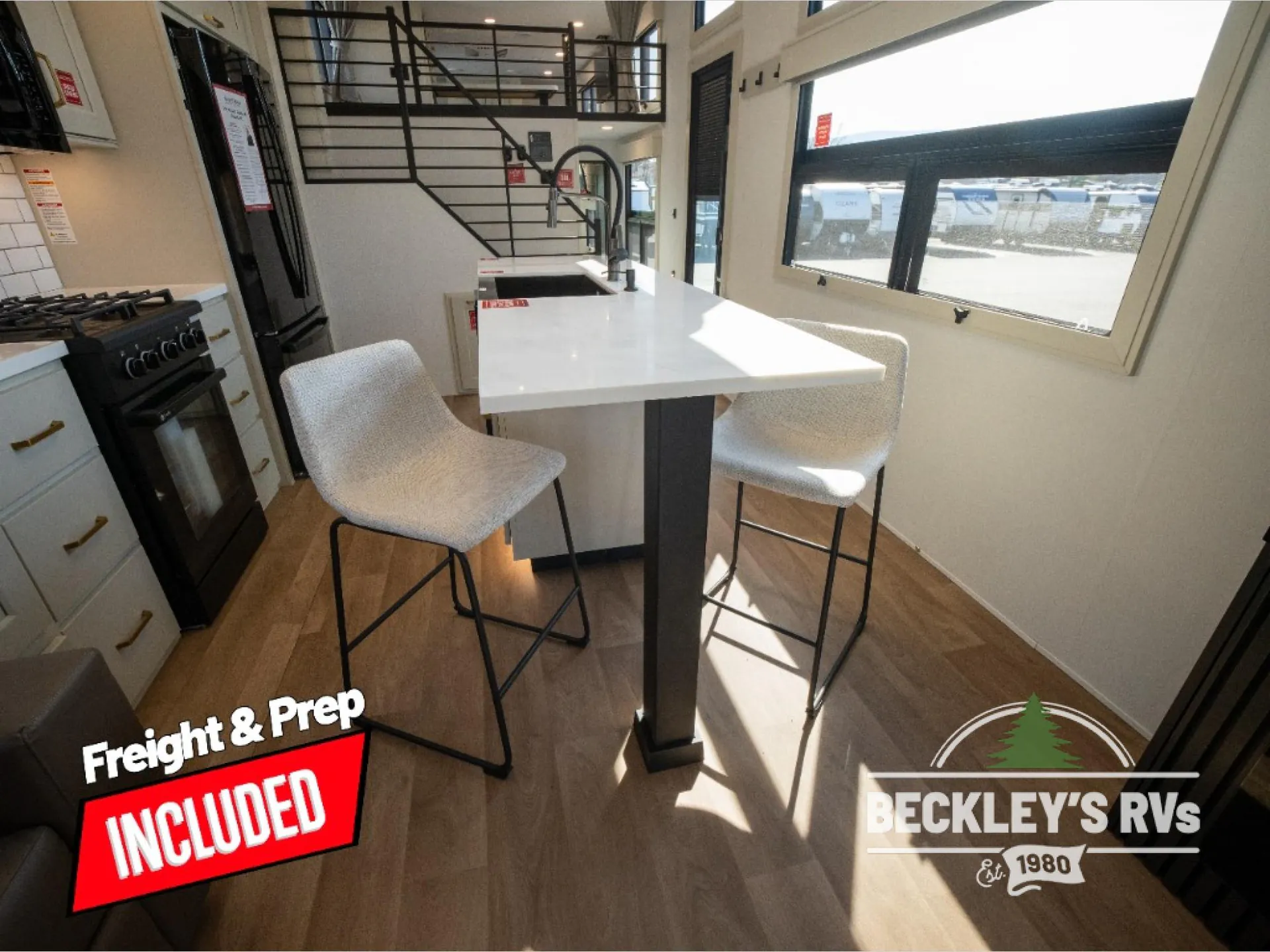 2026 Grand Design Foundation 42GD — Destination trailer dining counter with two stools beside the range, refrigerator, kitchen cabinetry, and visible loft stairs