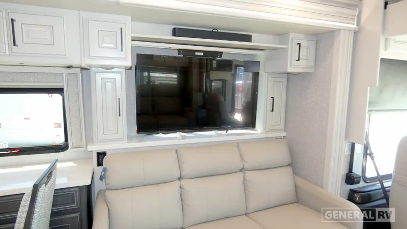 2027 Fleetwood Discovery LXE 40M — Living-area sofa beneath a large television, surrounded by overhead and side storage cabinets