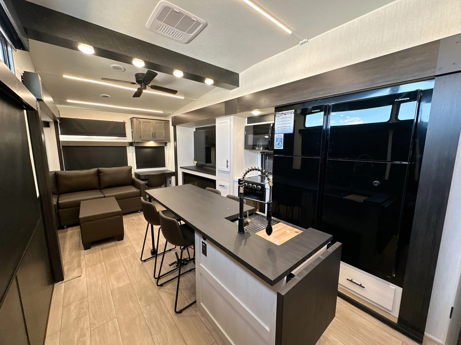 2026 Forest River Arctic Wolf 38LEAH.G — Fifth wheel kitchen with island sink, refrigerator, range, bar seating, adjacent dining table, and lounge sofa