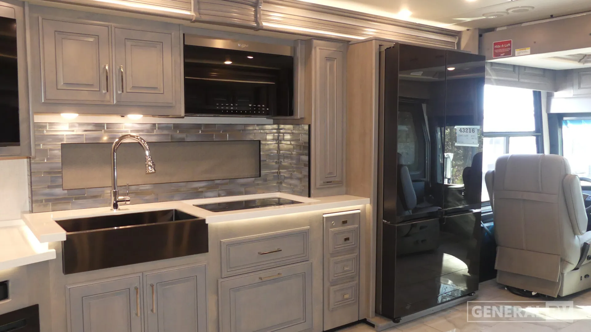 2026 Fleetwood Discovery LXE 40G — Kitchen with farmhouse sink, cooktop, microwave, backsplash, cabinetry, and refrigerator beside the cockpit entrance