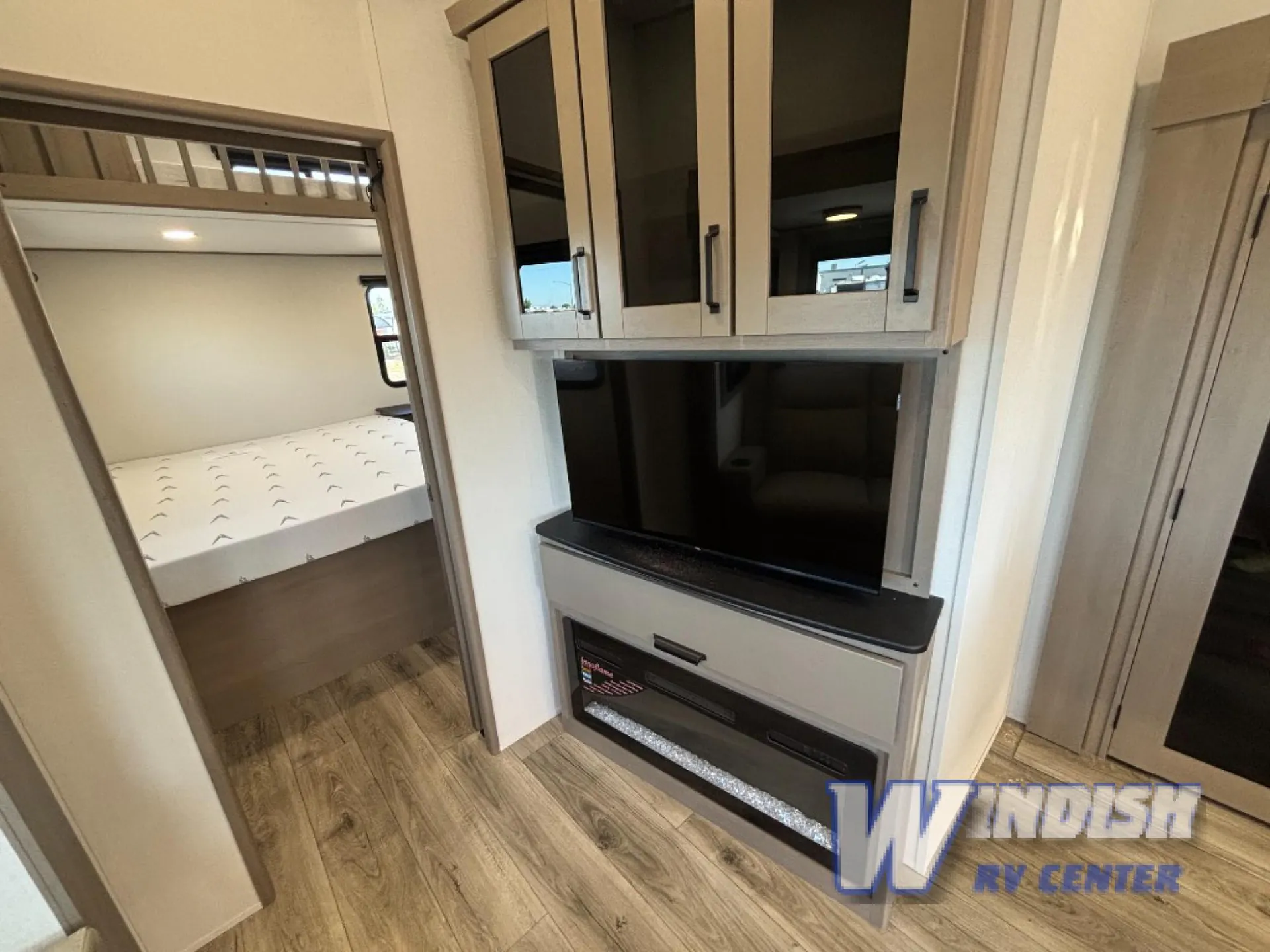 2027 Grand Design Reflection 362TBS — Living-area television and cabinetry beside an open doorway showing the main bed