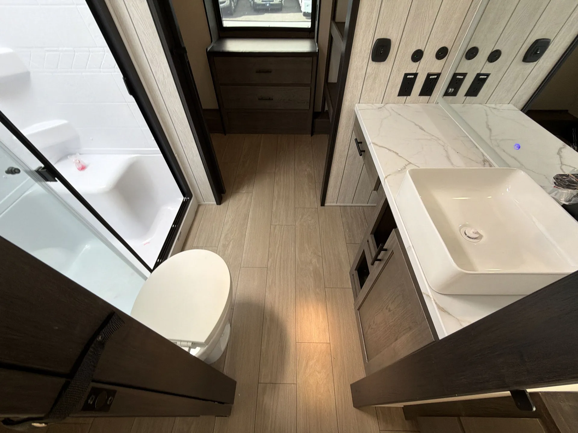 2026 Forest River Arctic Wolf 38LEAH.G — Bathroom view with a glass shower, toilet, vanity sink, mirrored cabinet, and hallway beyond