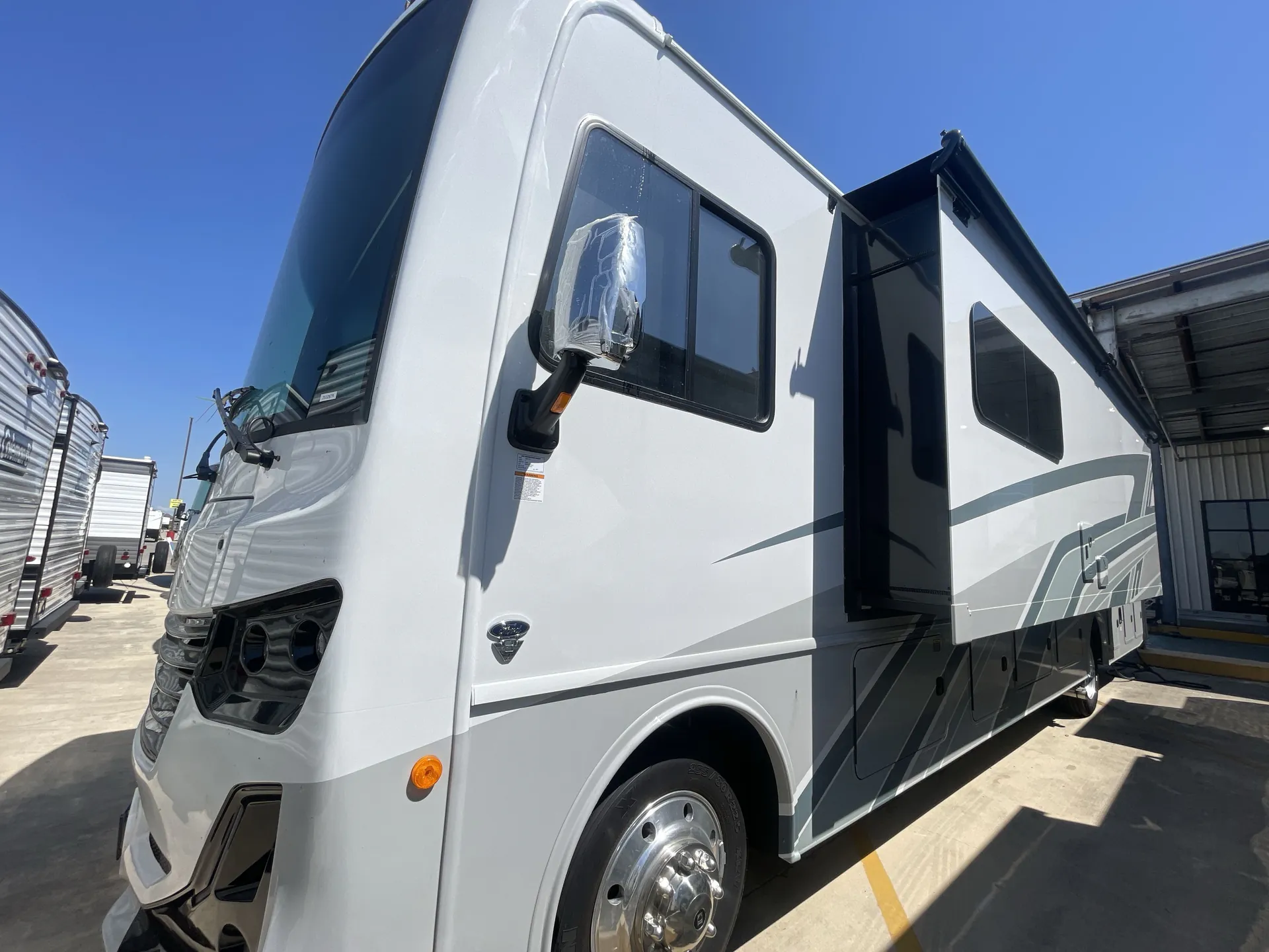 2026 Holiday Rambler Invicta 36Y — Front-side exterior photograph visibly shows the motorhome shell, cab, mirror, wheel, lights, and slide-out