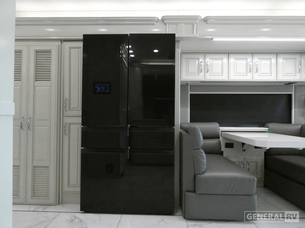 2026 American Coach American Dream 45A — Black refrigerator and tall cabinetry beside a dinette with booth seating and a table