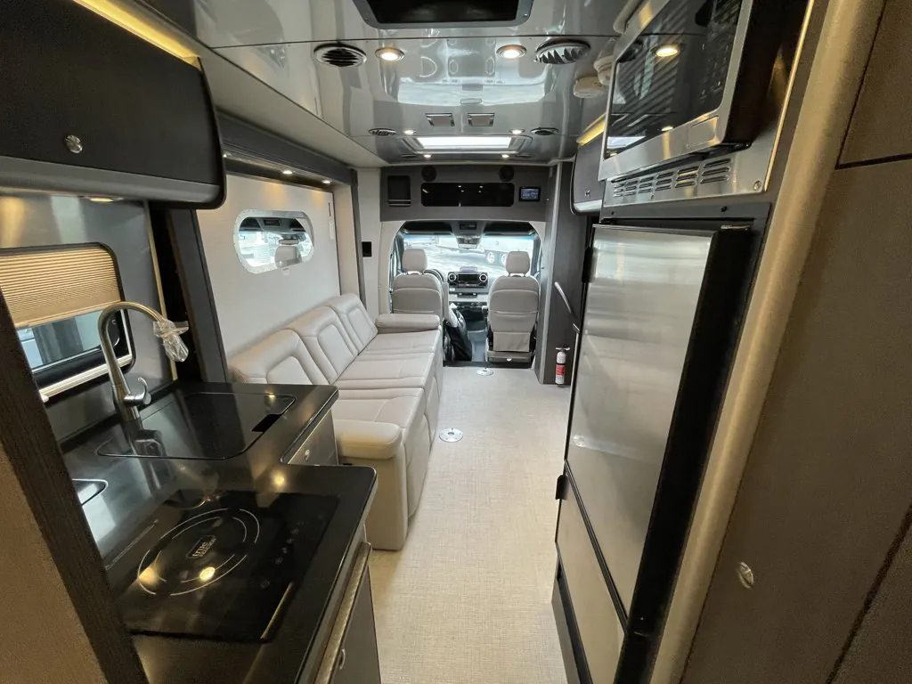 2026 Airstream Atlas Murphy Suite — Class B van interior with galley sink and cooktop, refrigerator, lounge seating, and visible cab controls