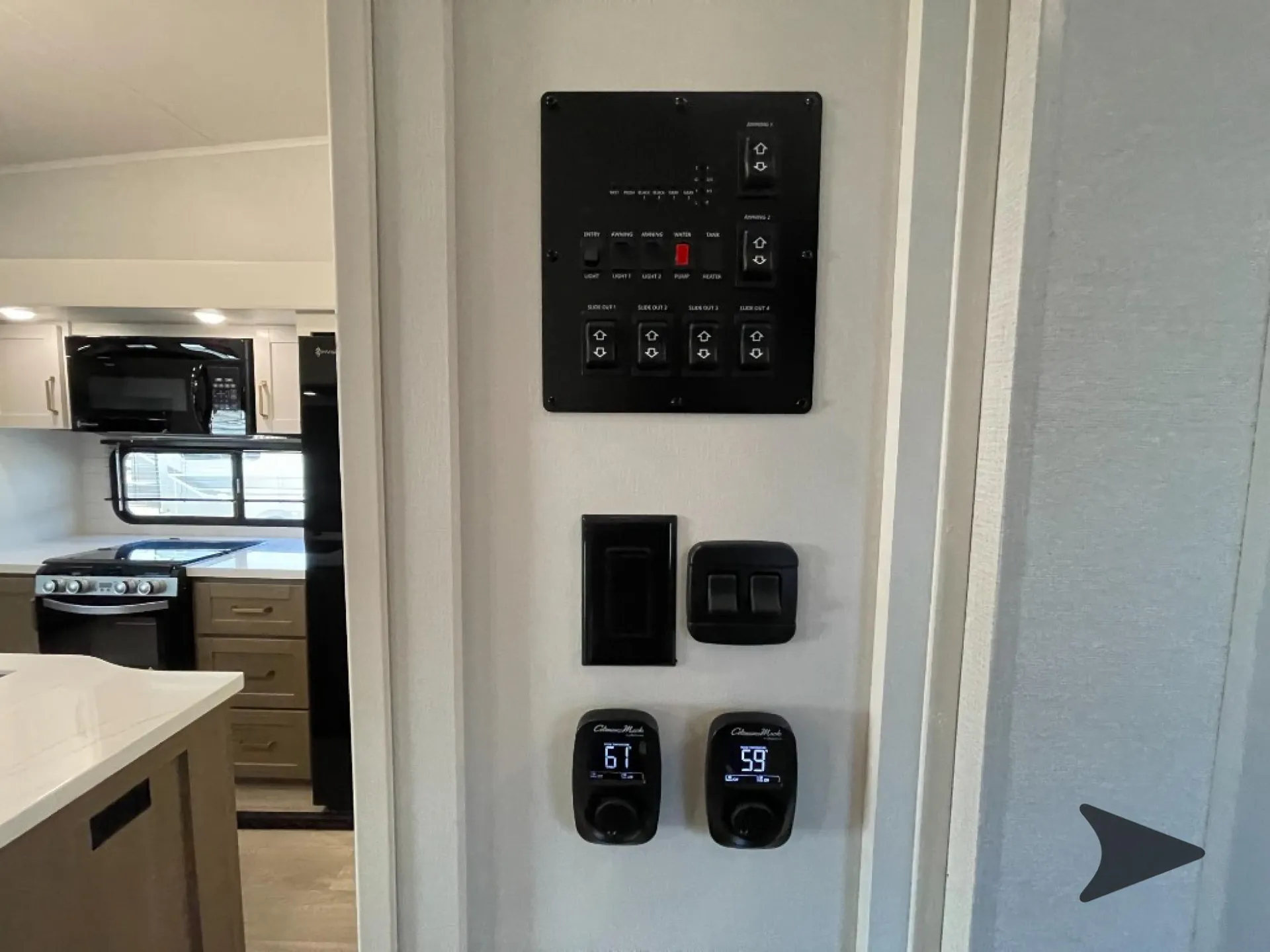 2027 Jayco Eagle 355MBQS — RV control panel and digital gauges beside a visible kitchen with range, microwave, refrigerator, and counter