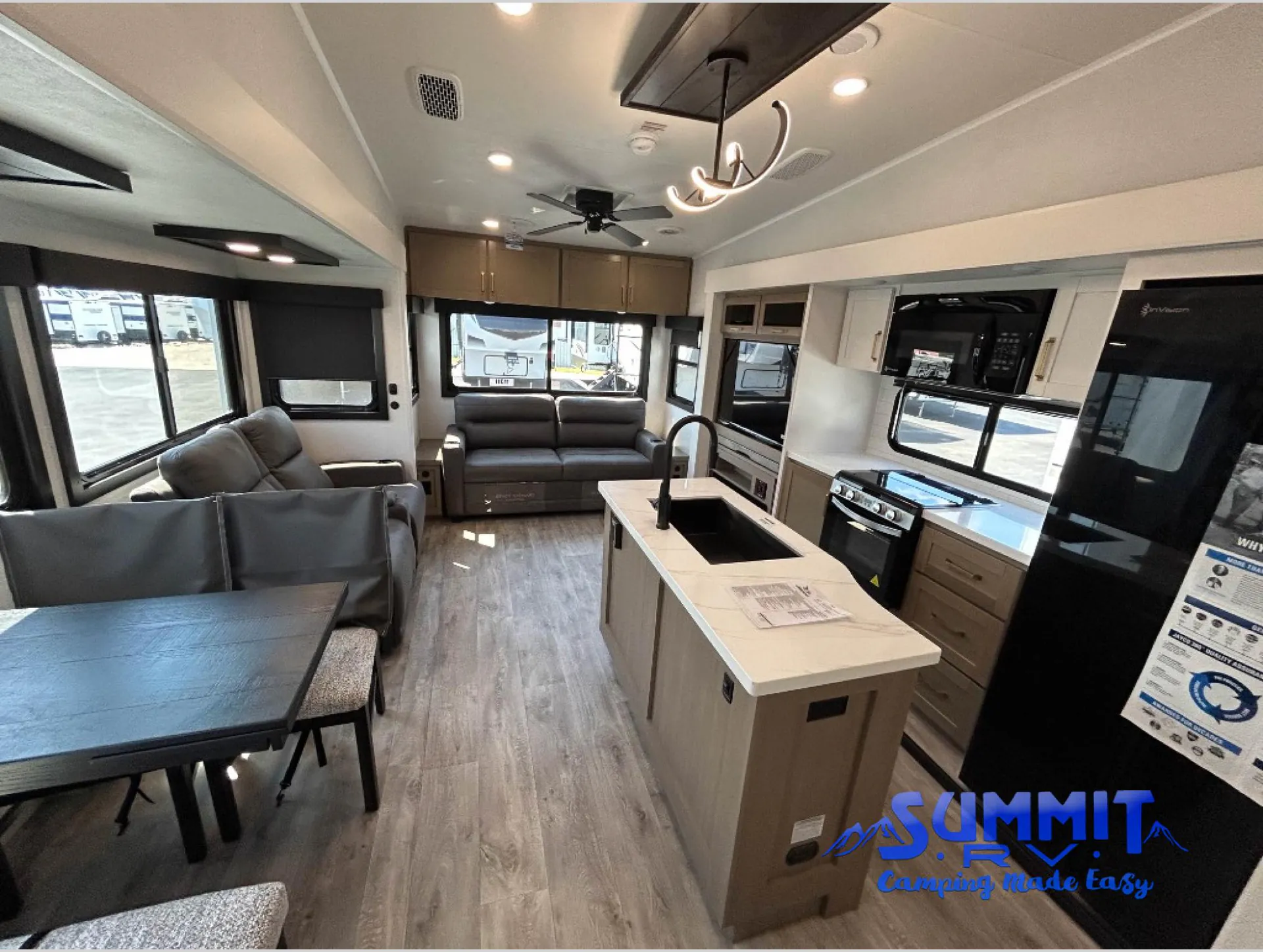 2027 Jayco Eagle 355MBQS — Kitchen island with sink beside dining table and lounge seating in an open fifth wheel interior