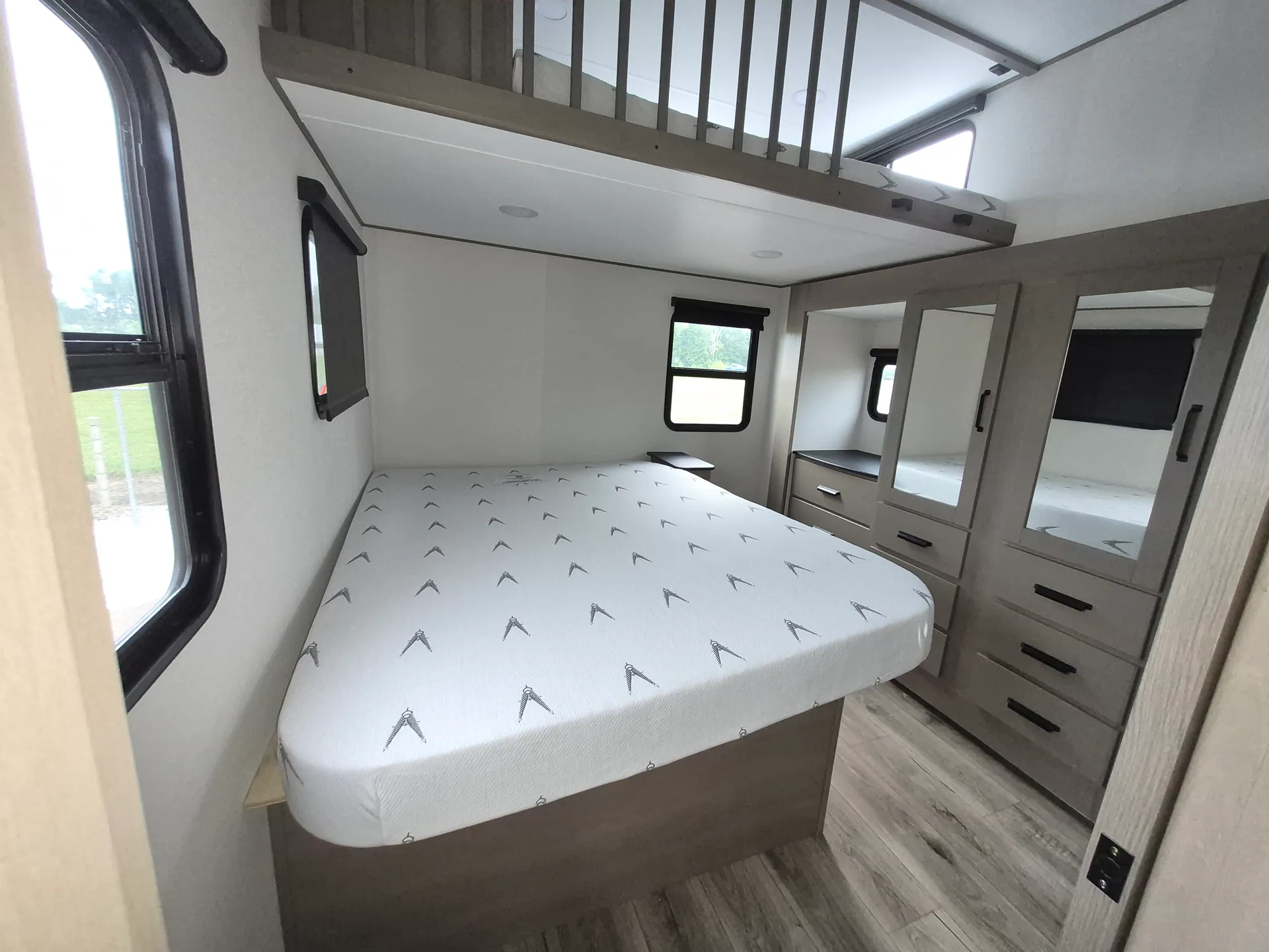 2027 Grand Design Reflection 362TBS — Main bedroom with a large bed, overhead storage platform, windows, dresser, and mirrored wardrobes