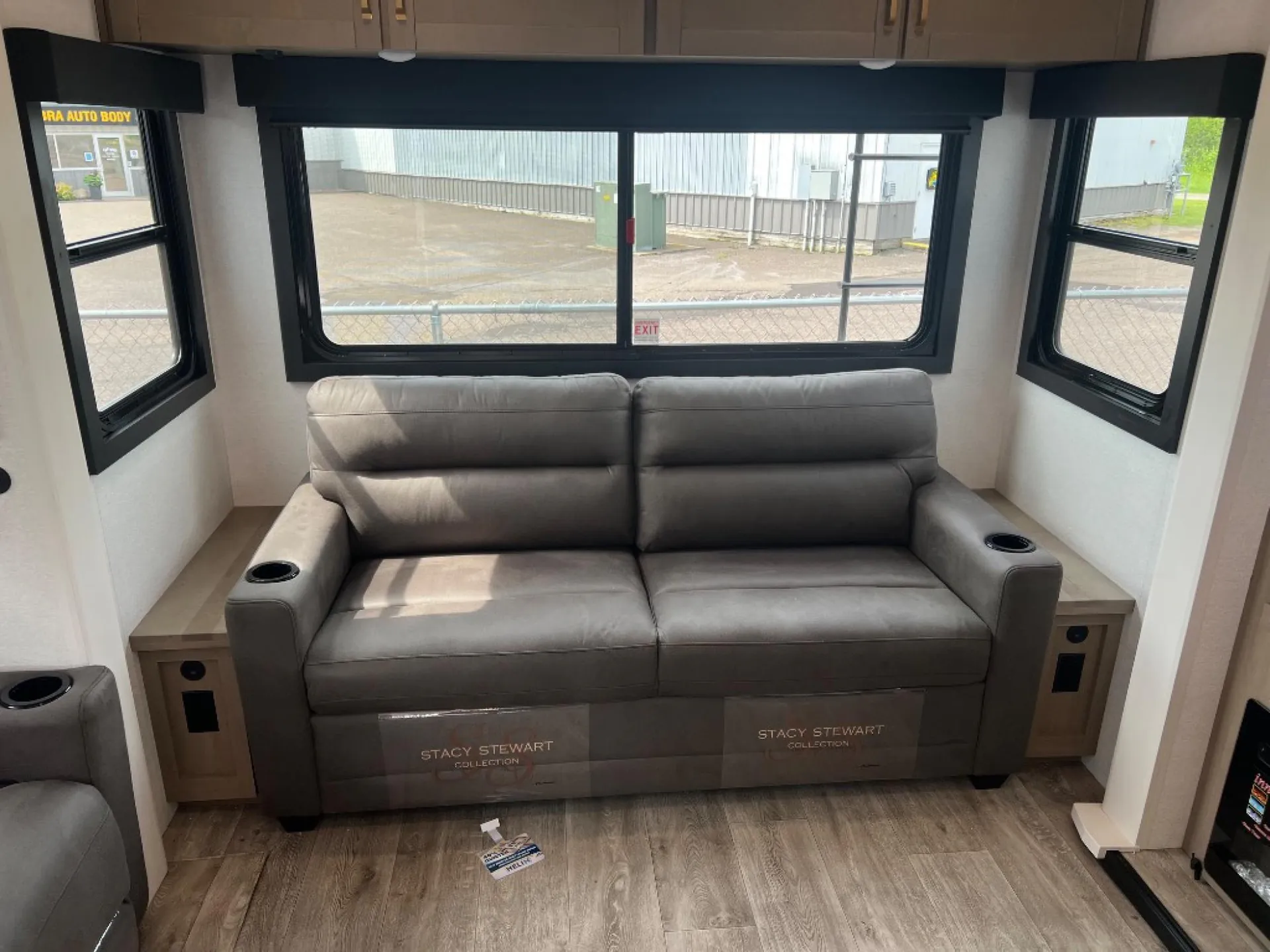 2027 Jayco Eagle 355MBQS — Gray reclining sofa centered beneath wraparound windows with side tables and cup holders in the lounge area
