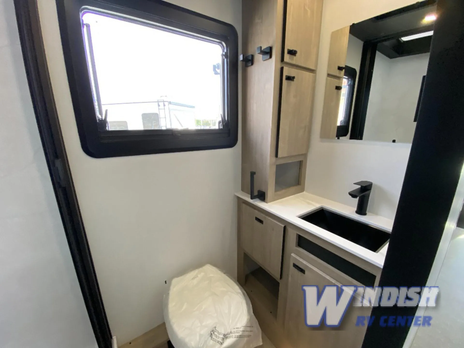 2027 Grand Design Lineage Series F 29AN5 — Motorhome bathroom with toilet, black sink, vanity cabinetry, mirror, and a bright side window