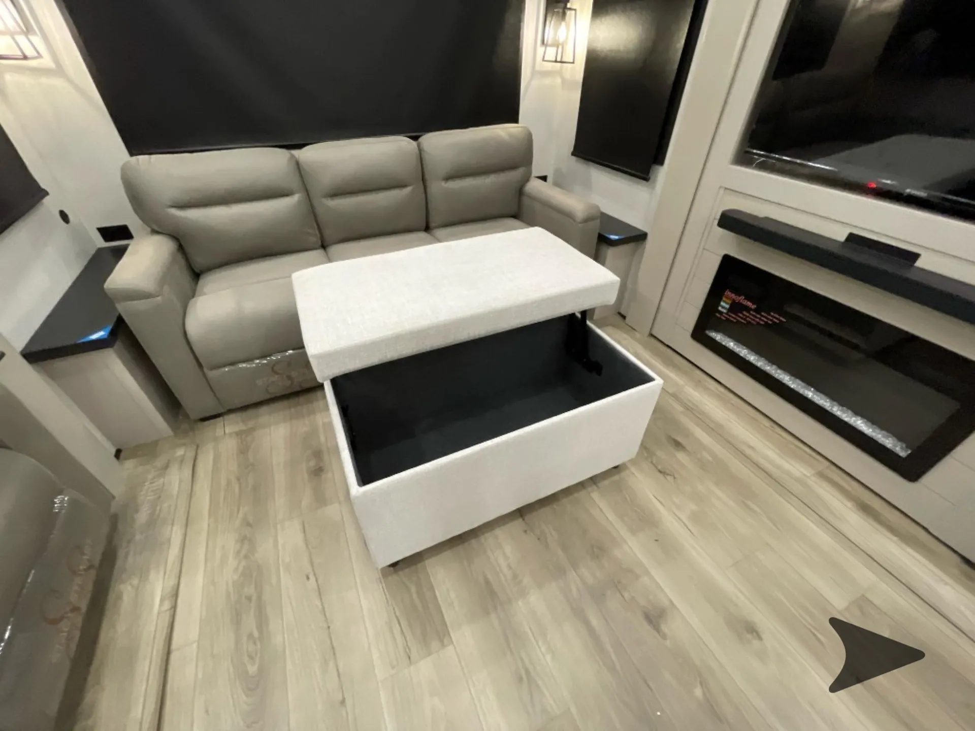 2026 Jayco North Point 377RLBH — Living area with a three-seat recliner sofa, lift-top storage ottoman, blackout shades, and electric fireplace entertainment wall