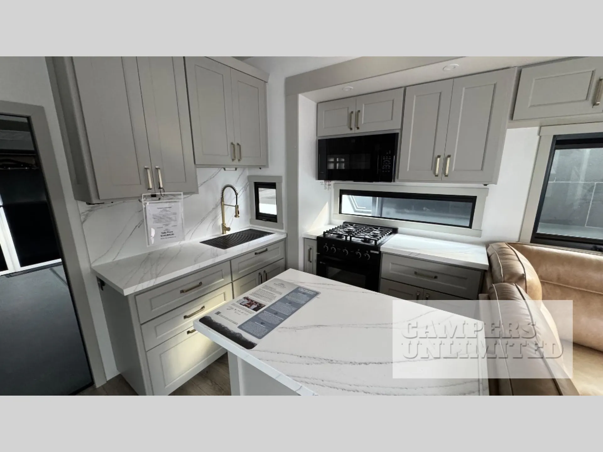 2026 Brinkley Model G 3950 — Kitchen sink, faucet, range, microwave, island, and cabinetry are shown beside the edge of a leather sofa