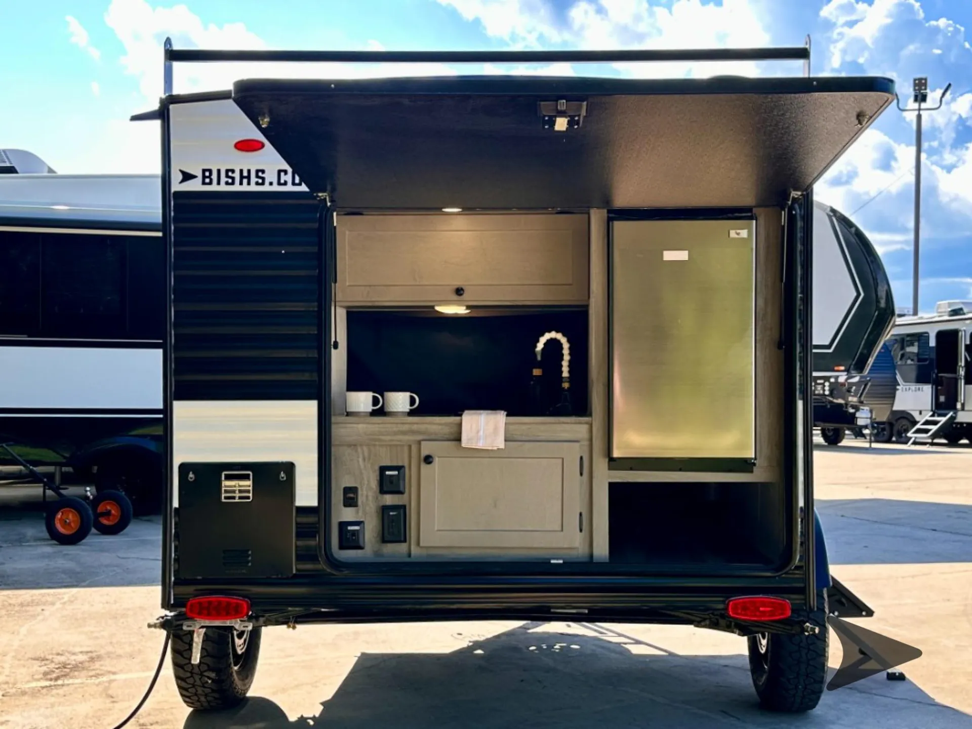 2026 Wayfinder Go Lite Solo — Photograph of the exterior galley hatch open; the visible installed sink, faucet, counter, cabinets, and refrigerator are kitchen equipment