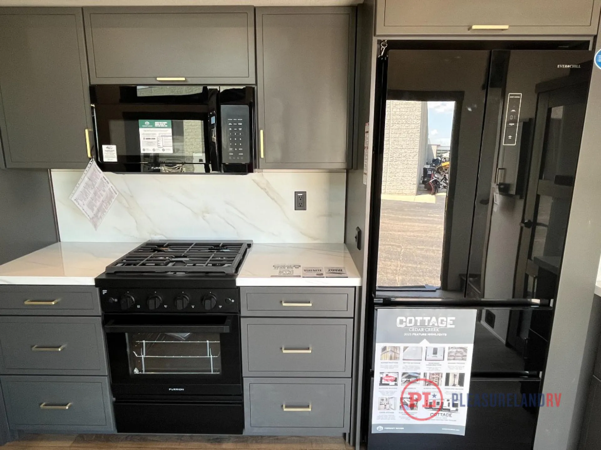 2025 Forest River Cedar Creek Cottage 41FWC — Fifth wheel kitchen with gas range, microwave, refrigerator, backsplash, countertops, and surrounding dark cabinetry