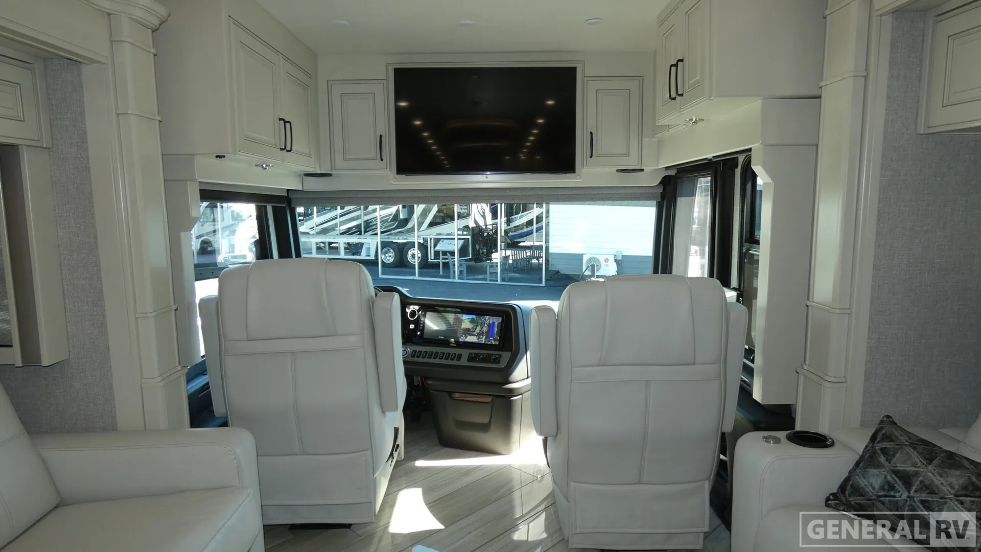 2026 American Coach American Dream 45A — Class A cockpit with dashboard, two captain's chairs, overhead television, and adjacent white lounge seating
