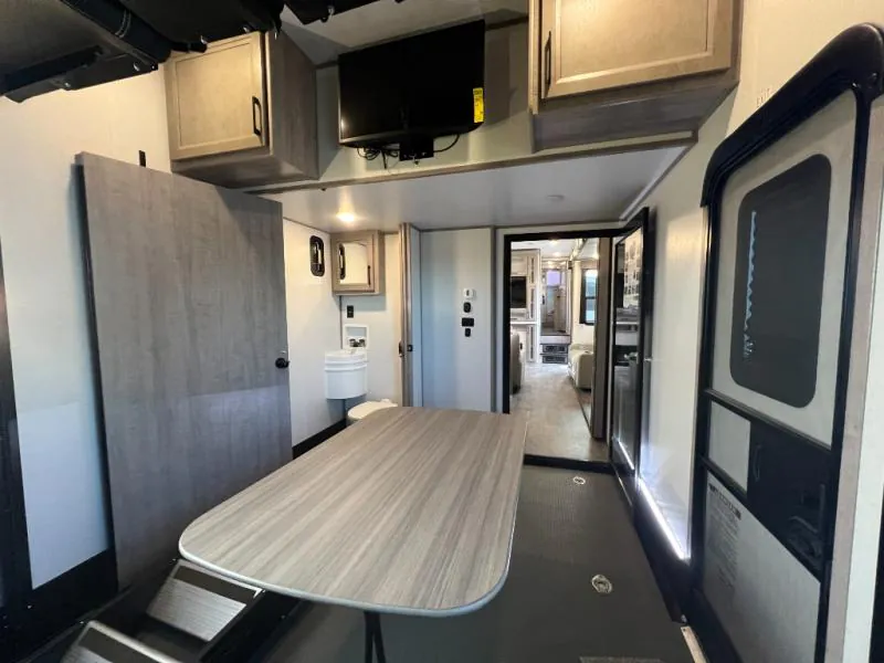 2023 Dutchmen Voltage 4225 — Garage dining table in the foreground, with overhead cabinets and television, opening toward the fifth wheel living interior