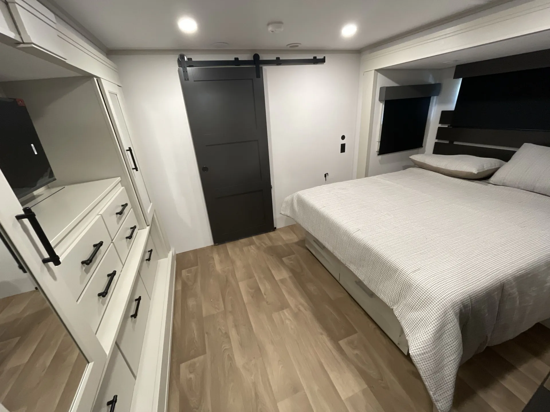 2026 Grand Design Solitude 391DL — Main bedroom with a bed, dresser, television, overhead storage, and sliding entry door