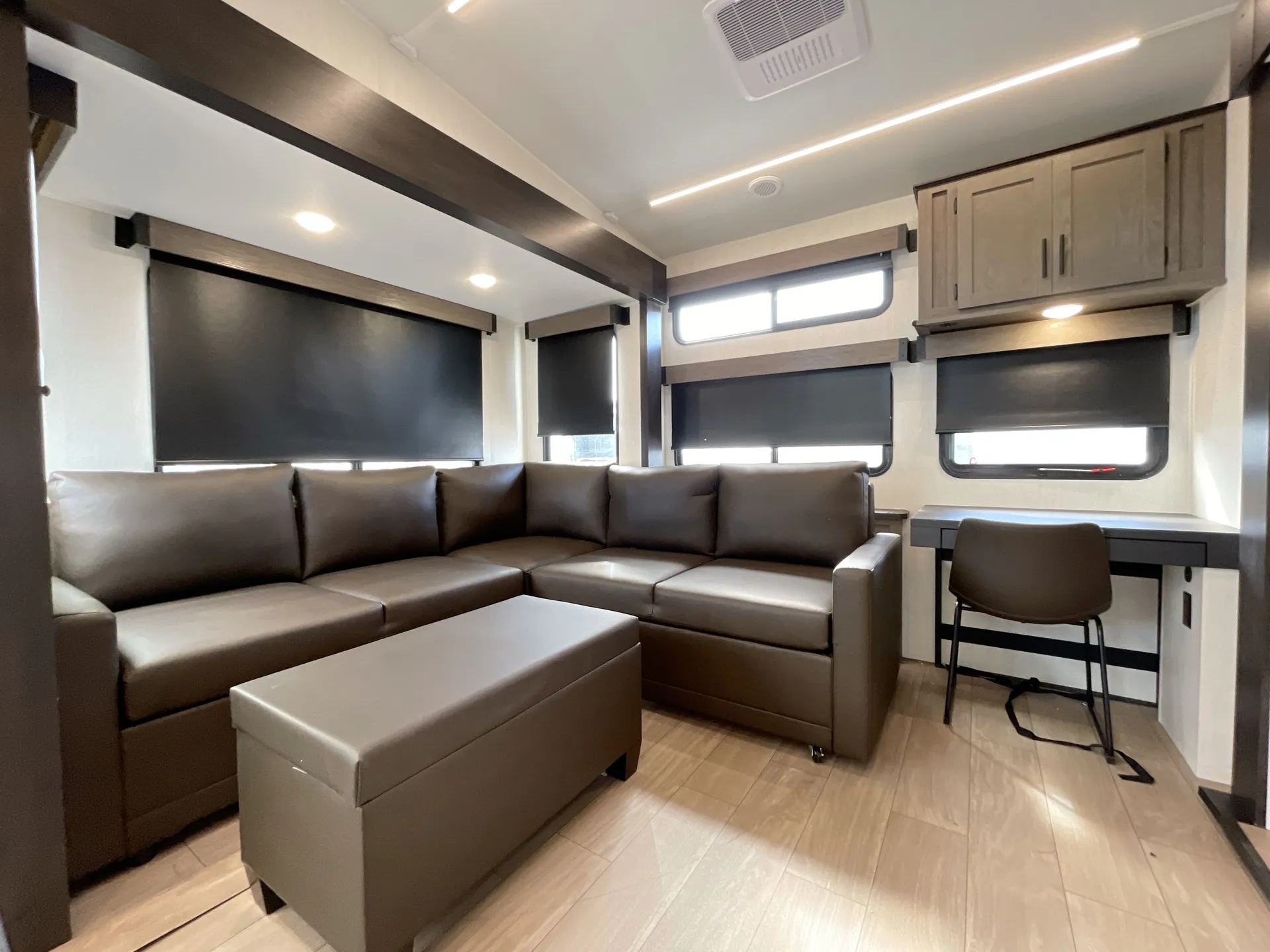 2026 Forest River Arctic Wolf 38LEAH.G — Fifth wheel living area with an L-shaped leather sofa, ottoman, windows, desk, and overhead cabinets