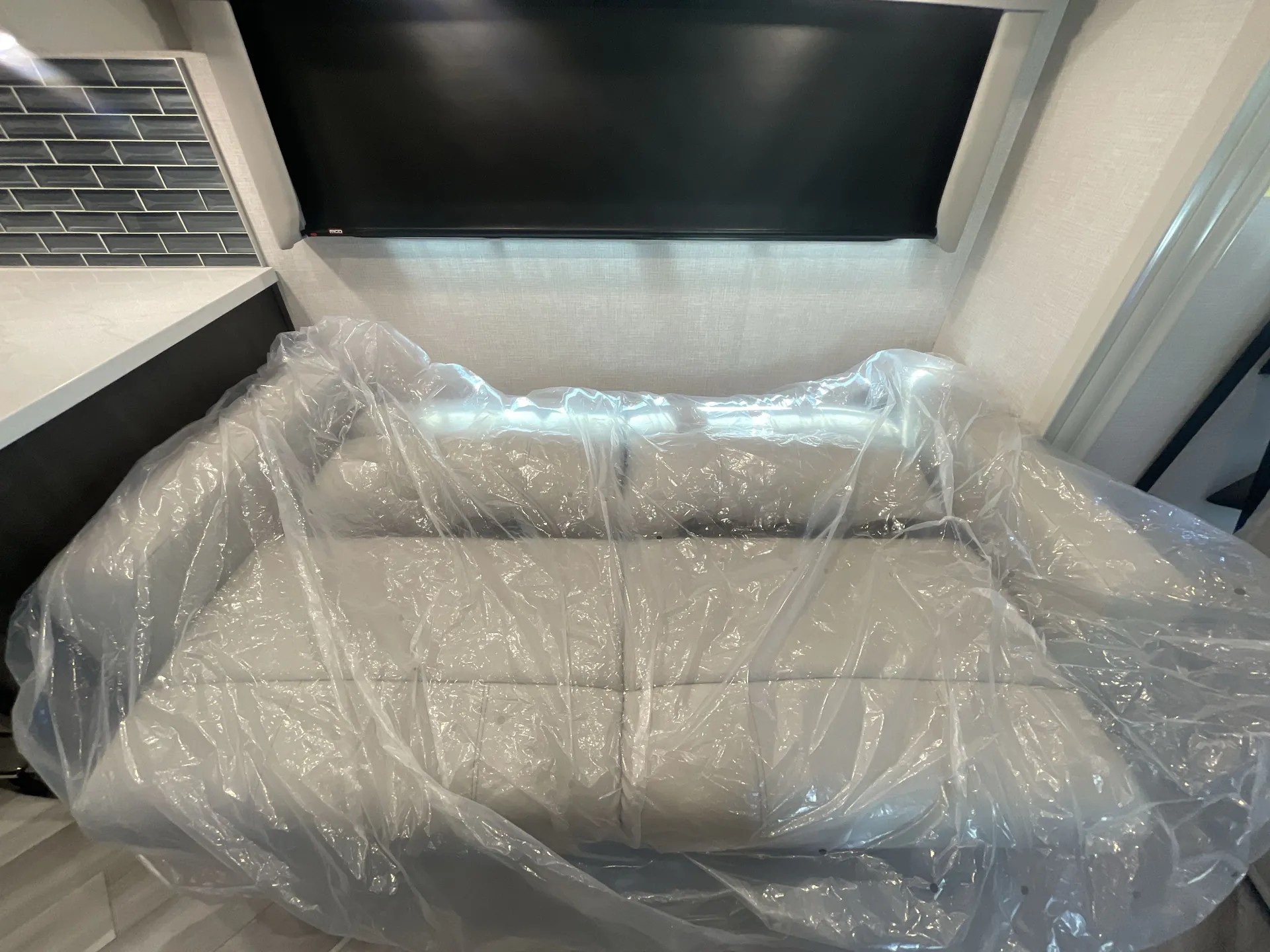 2026 Holiday Rambler Invicta 36Y — Plastic-wrapped living sofa positioned beneath a large wall-mounted television
