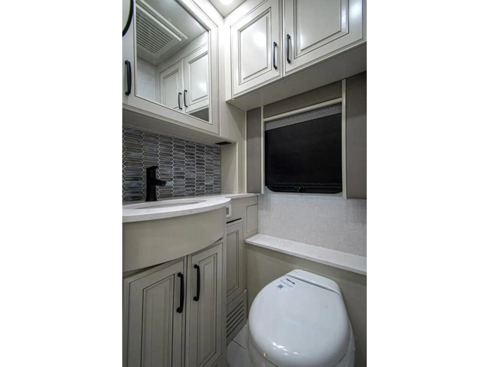 2026 American Coach American Dream 45A — Bathroom vanity with black faucet, toilet, upper cabinets, and a wall-mounted television