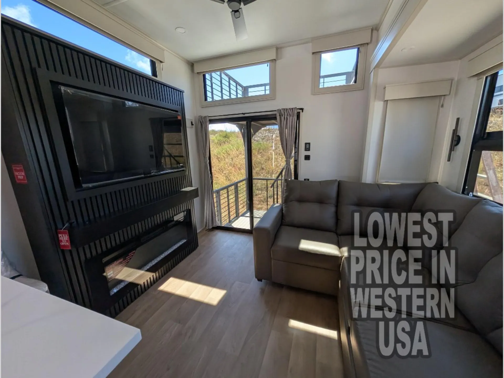 2026 Grand Design Foundation 42GD — Destination trailer living area with sectional seating, wall-mounted television, fireplace, windows, and glass deck door