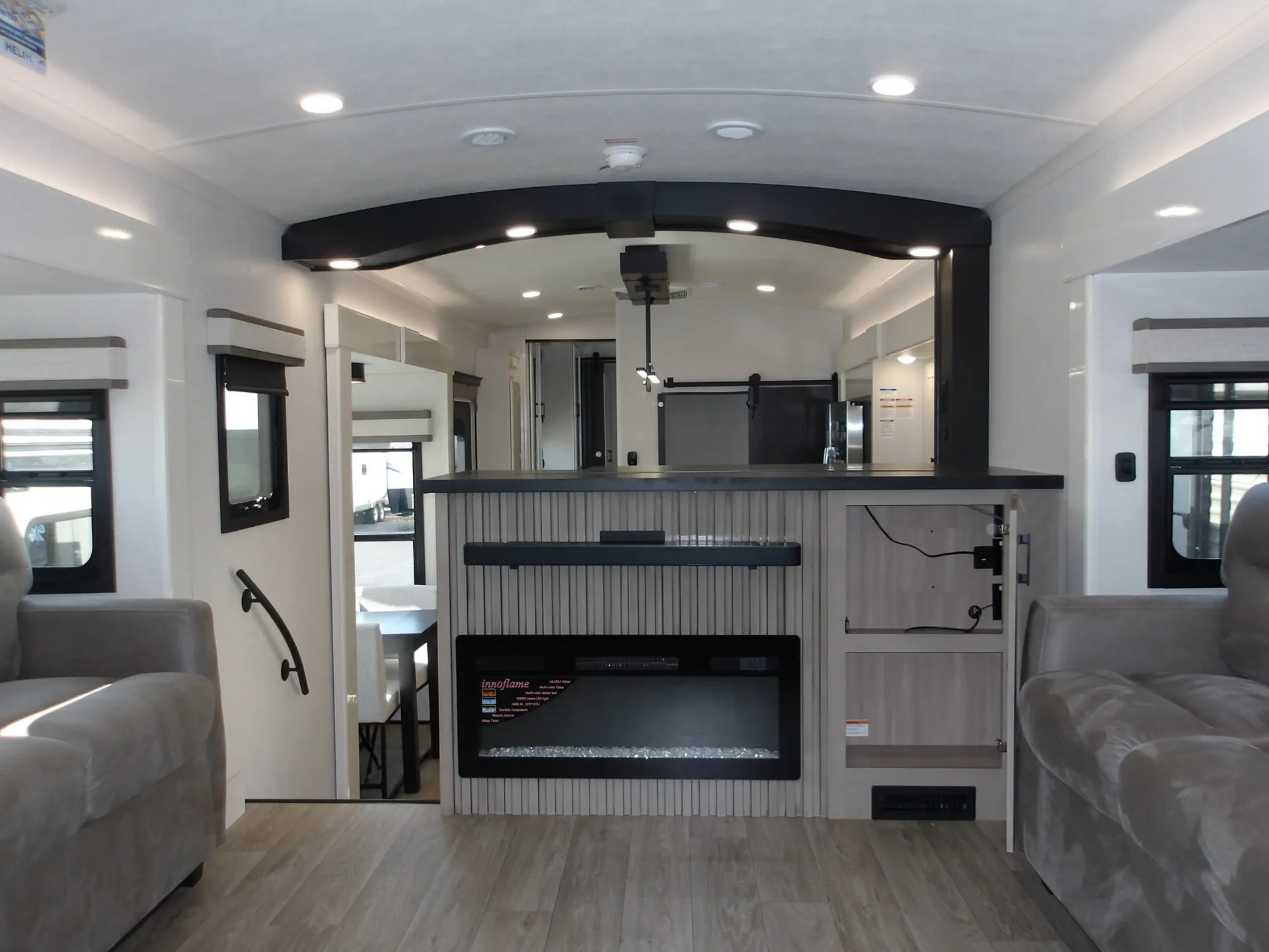 2027 Jayco Pinnacle 39FLOK — Fifth wheel lounge overview with fireplace, open media cabinetry, kitchen peninsula, and dinette beyond