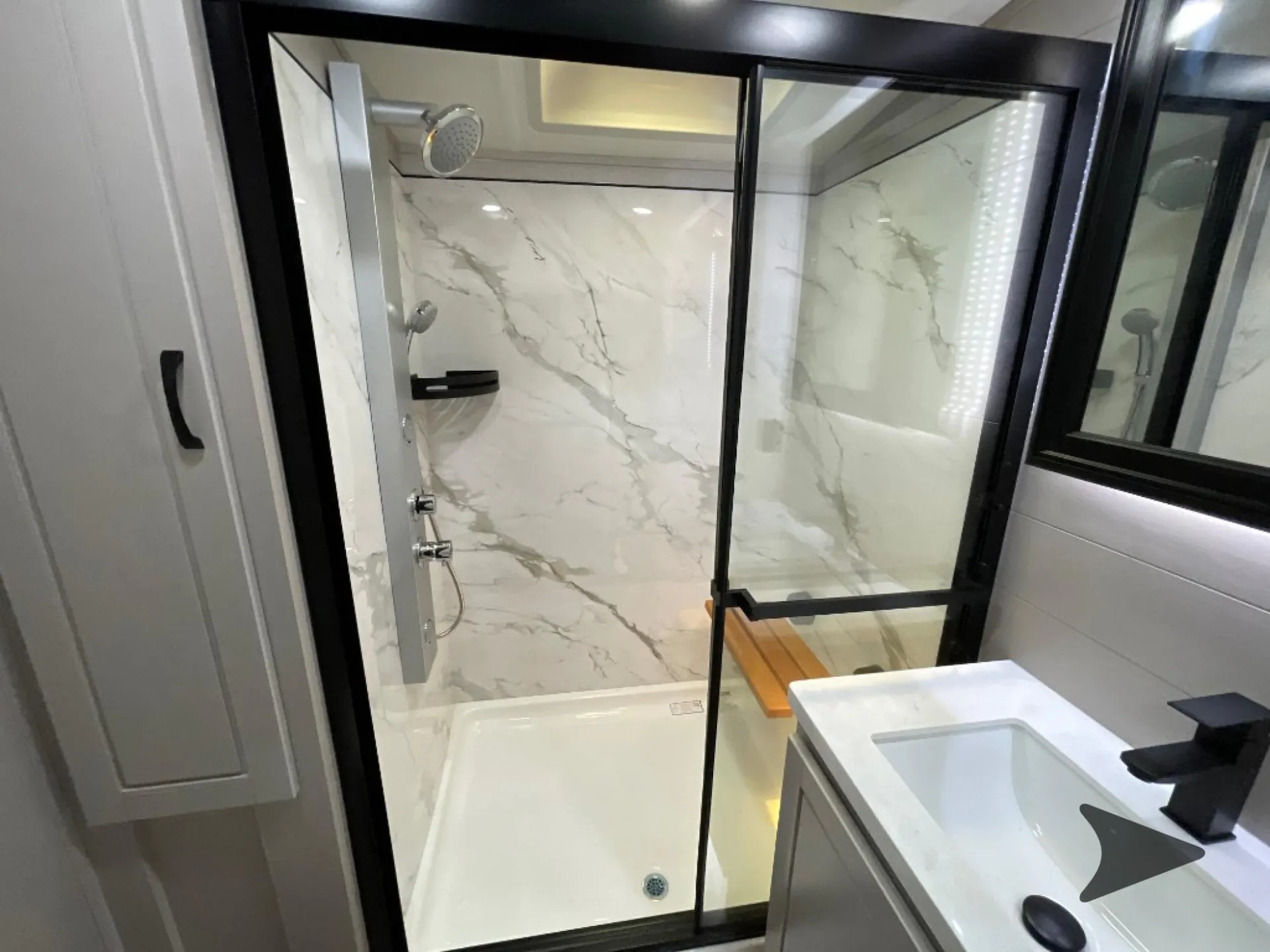 2026 Jayco North Point 377RLBH — Bathroom shower with glass doors, marble-pattern wall panels, handheld fixtures, and adjacent vanity sink