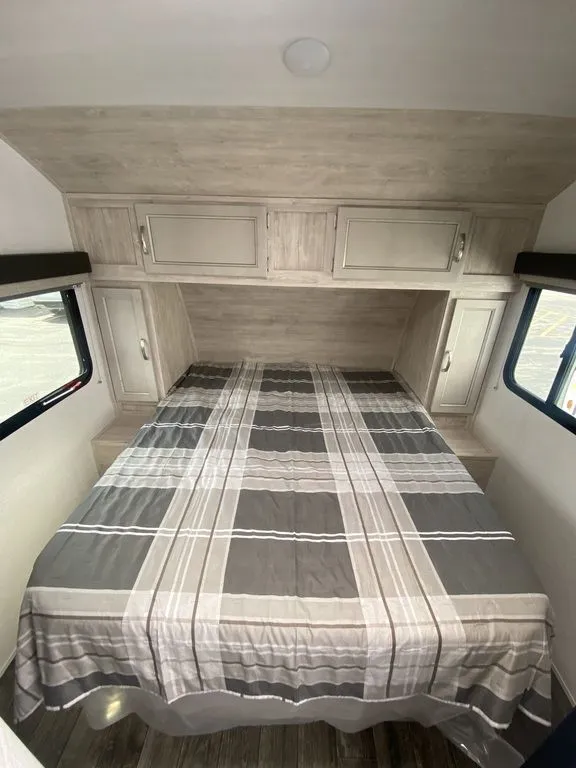 2026 Gulf Stream Vista Cruiser 19ERD — Main bed in an enclosed travel trailer bedroom with overhead cabinets, side wardrobes, windows, and wood-look walls