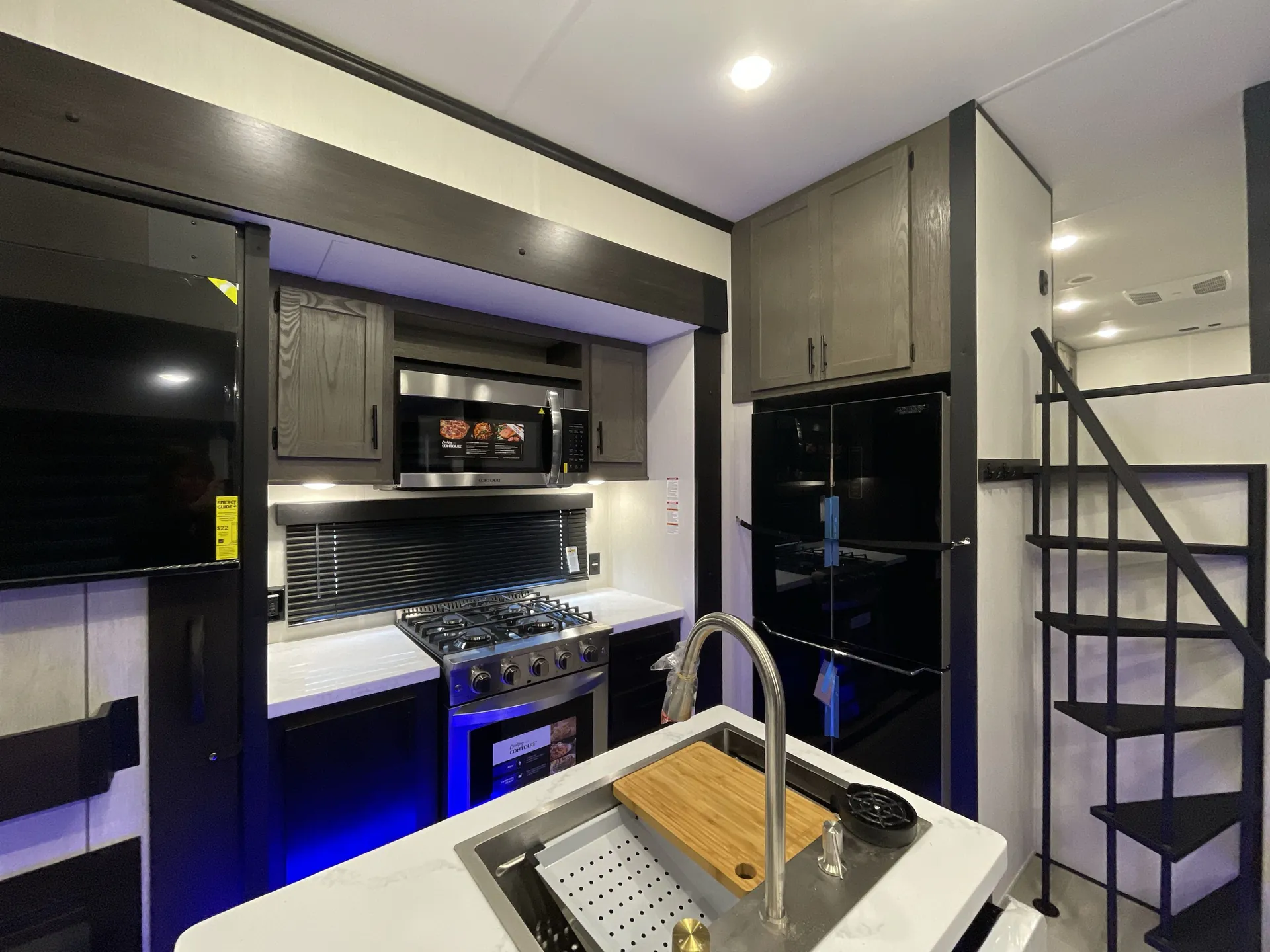 2026 Forest River Cherokee Wolf Pack 397STAY — Travel trailer kitchen with island sink, gas range, microwave, refrigerator, and ladder to an overhead loft