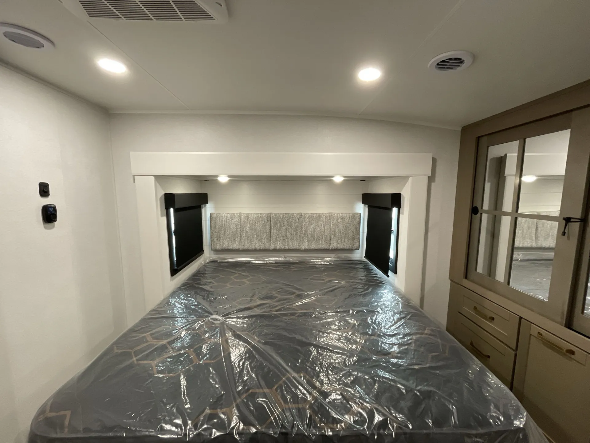 2027 Jayco Eagle 355MBQS — Fifth wheel main bedroom with a plastic-covered bed, side windows, and mirrored wardrobe dresser